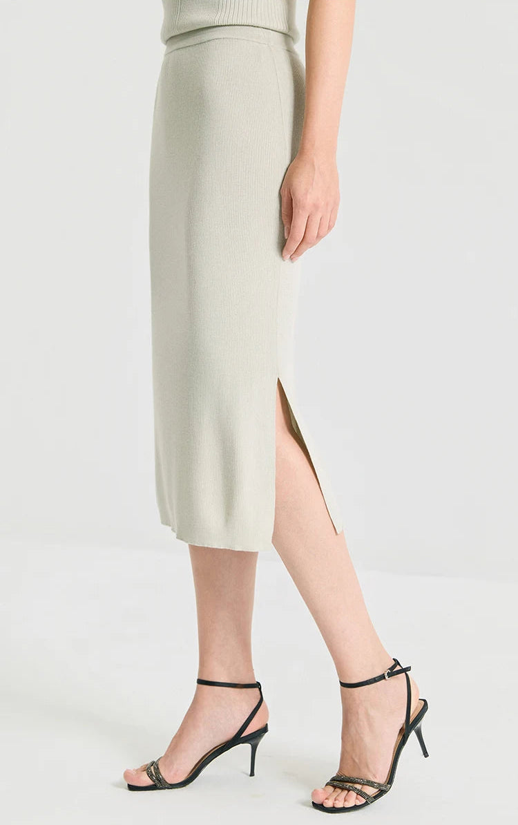 Left side profile view of a model in the mid-calf length rib knit wool-silk skirt in Compliant Sage green. From Borcelleclothes.
