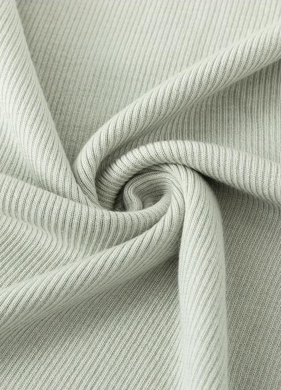 A close-up shot of the dense, matte wool-silk fabric in Compliant Sage green, artfully folded in a spiral to showcase the texture of the rib knit. From Borcelleclothes.