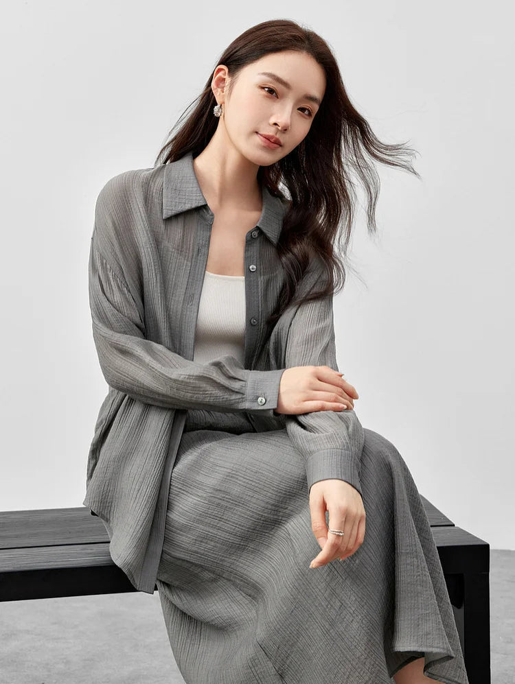 A woman sitting on a bench wearing a semi-sheer graphite rain lyocell two-piece set. — From Borcelleclothes.