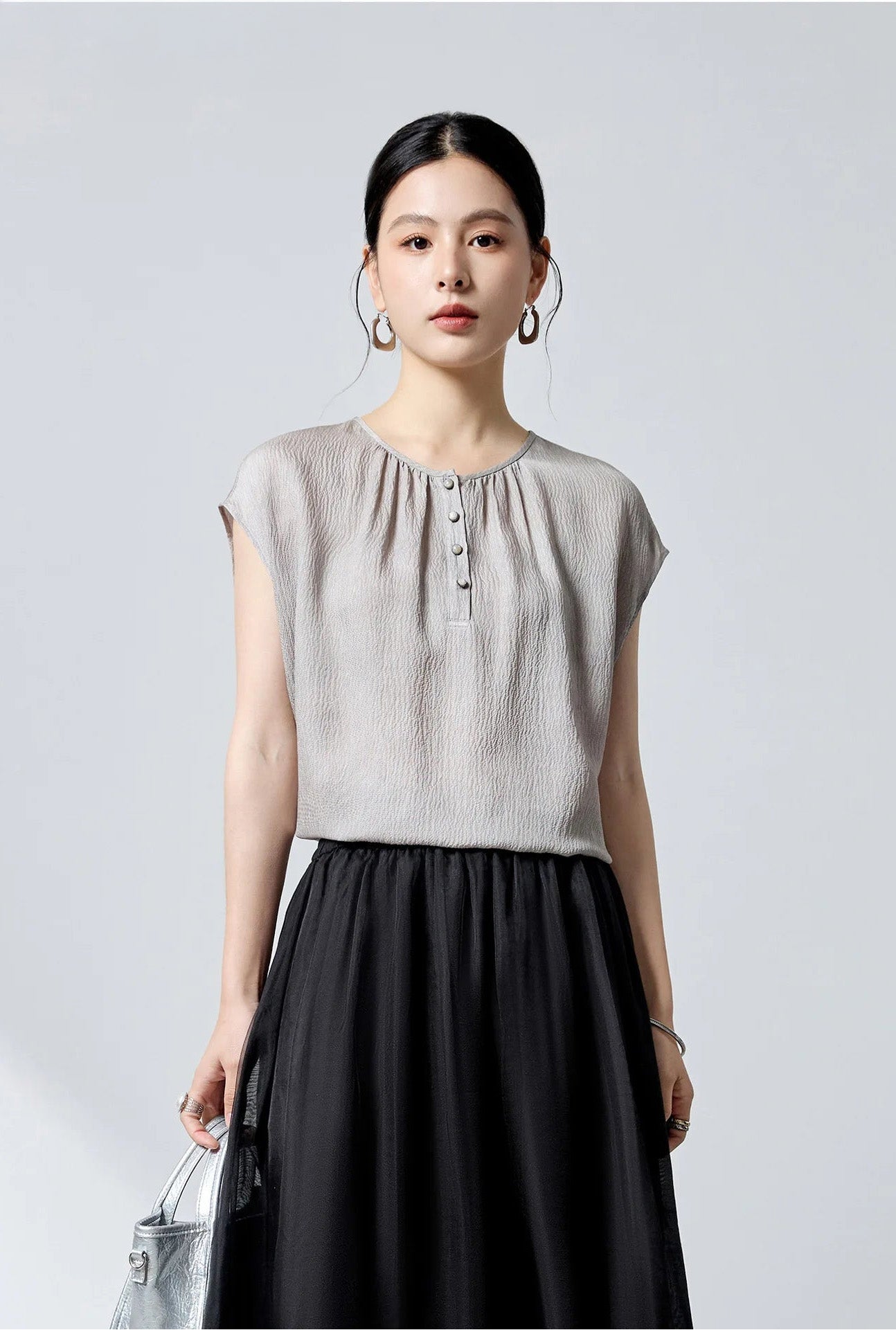Close-up of model wearing the Where Lives Nacre silk blouse and holding a matching accessory. — From Borcelleclothes.
