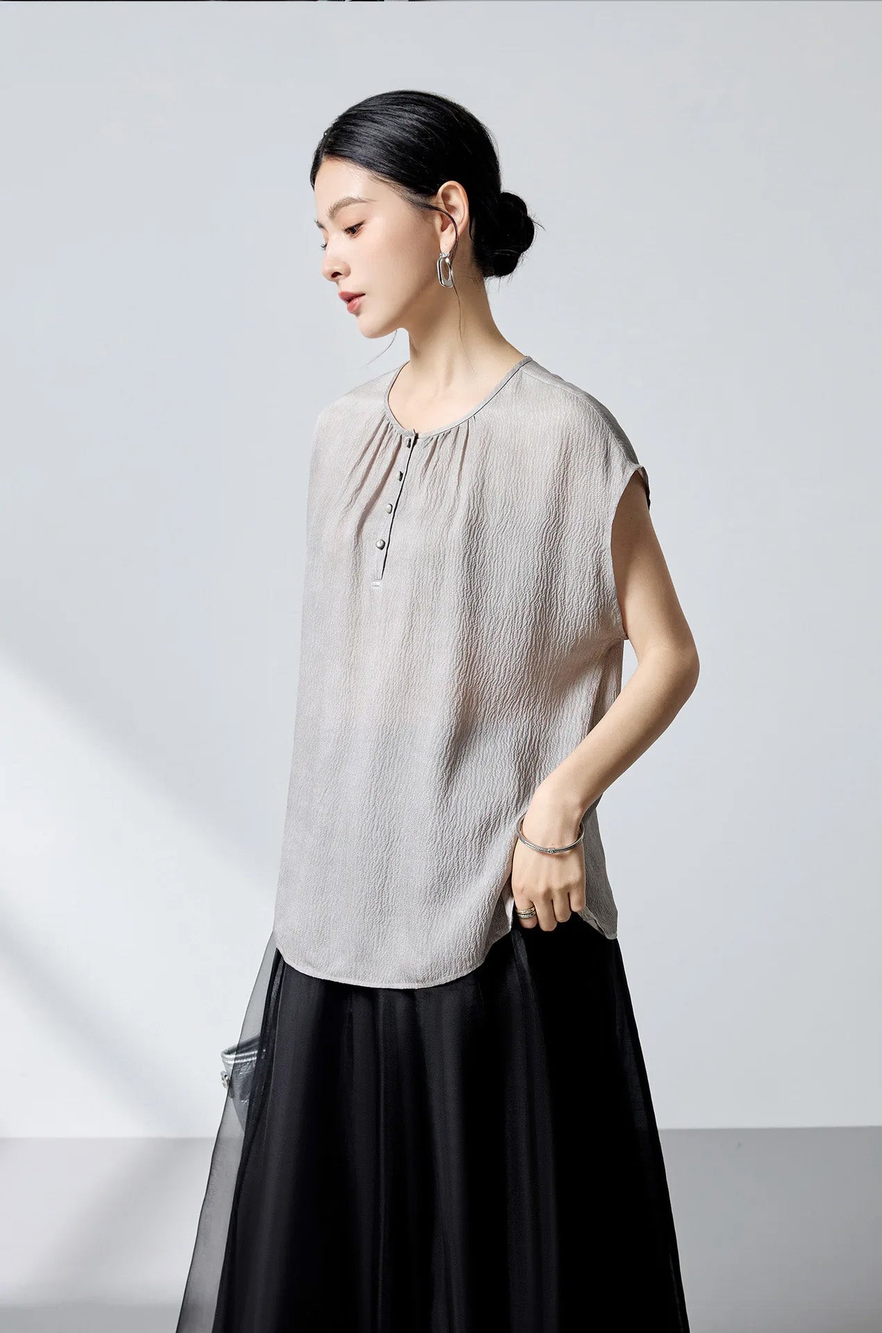 Model slightly lifting the hem of the Where Lives Nacre silk georgette blouse to show drape and side slit. — From Borcelleclothes.