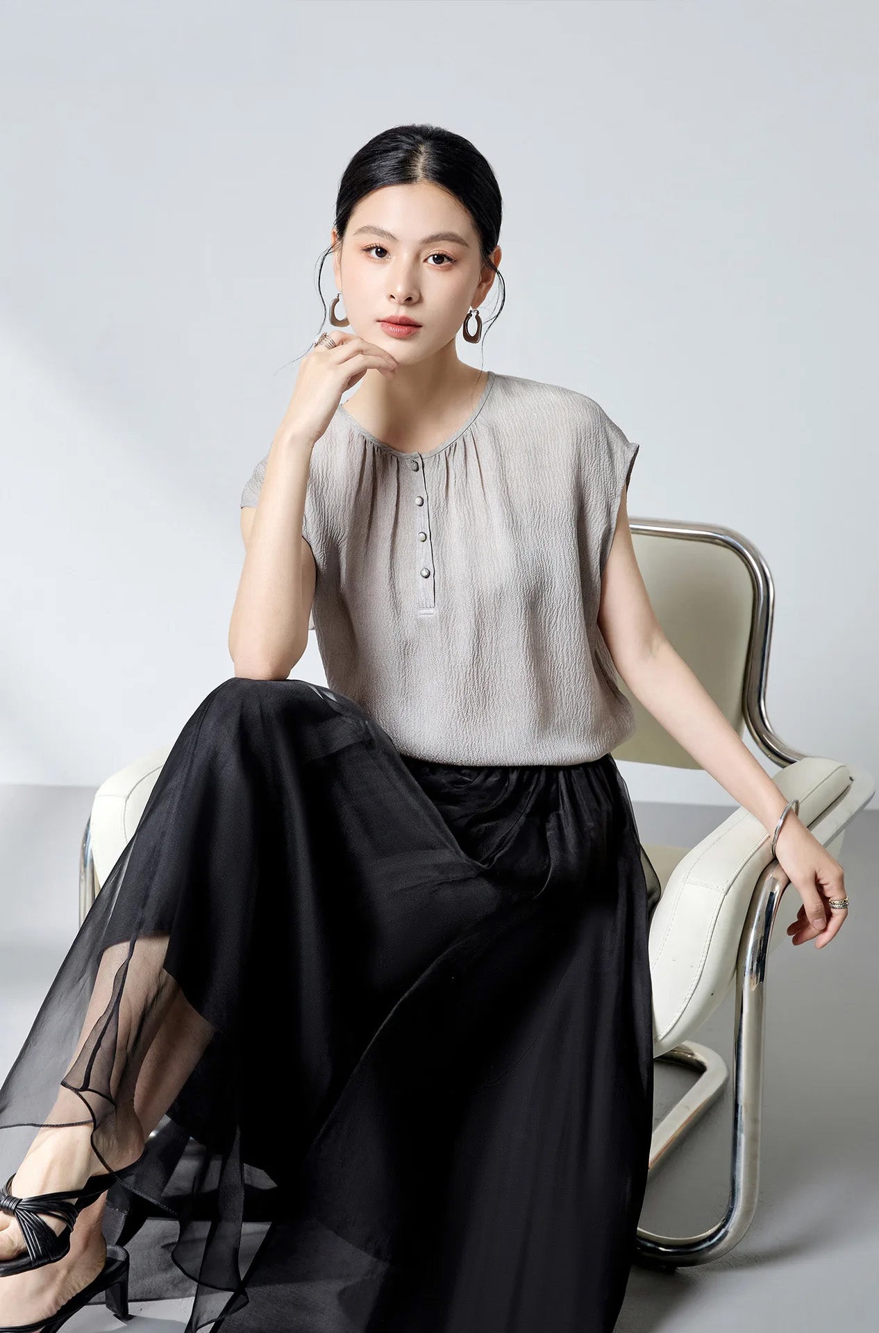 Model seated in an armchair wearing the loose-fitting silk georgette blouse in Where Lives Nacre. — From Borcelleclothes.