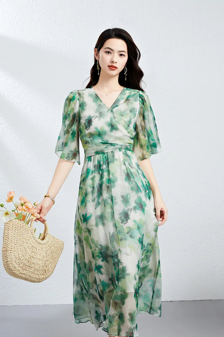 A woman holding a woven bag with flowers, wearing a Jade Breeze silk georgette flutter sleeve dress that mirrors the natural botanical motif — From Borcelleclothes.