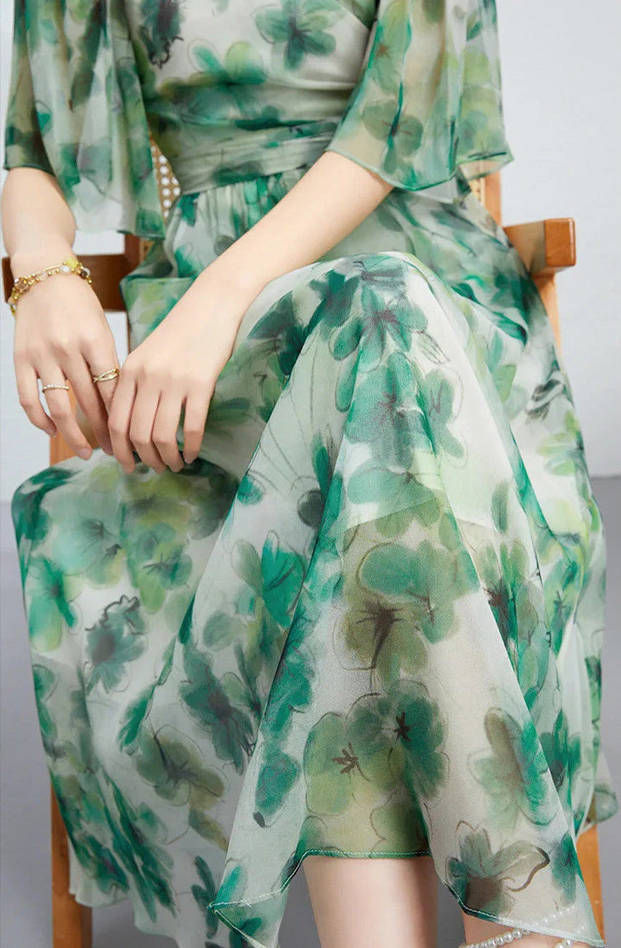 A seated woman in a Jade Breeze silk georgette dress touching her fingertips, highlighting the delicate watercolor emerald patterns — From Borcelleclothes.