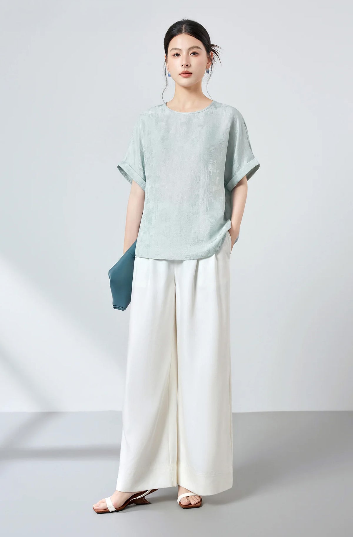 Full-length styling of a Glacial Spring silk Sangbo blouse with model holding a blue clutch and one hand in white pant pocket — From Borcelleclothes.