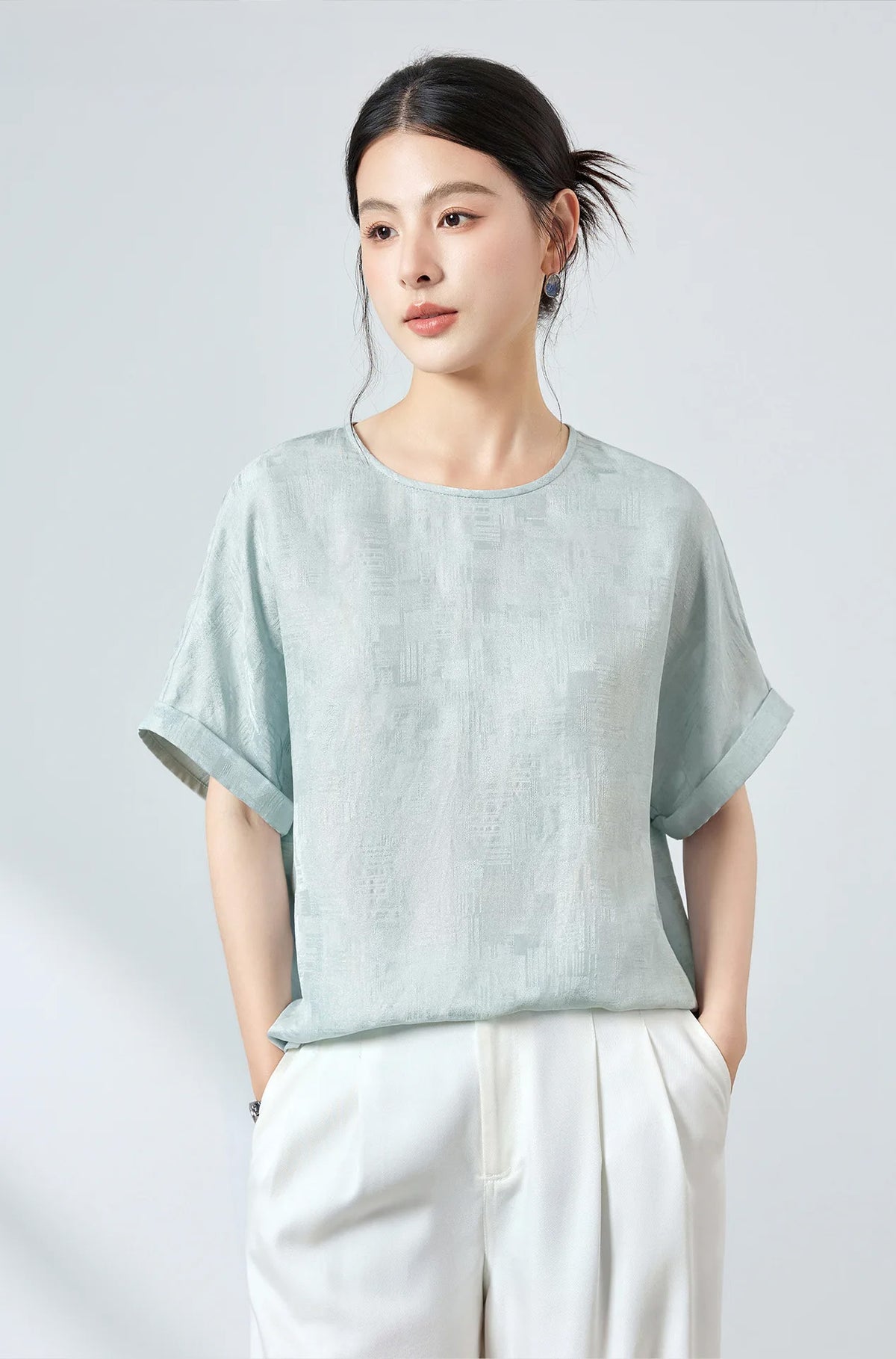 Front view of model in a Mulberry silk Sangbo jacquard blouse in Glacial Spring shade with hands resting in white trouser pockets — From Borcelleclothes.