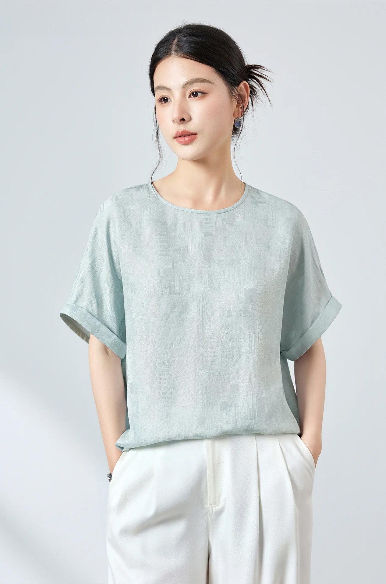 Front view of model in a Mulberry silk Sangbo jacquard blouse in Glacial Spring shade with hands resting in white trouser pockets — From Borcelleclothes.