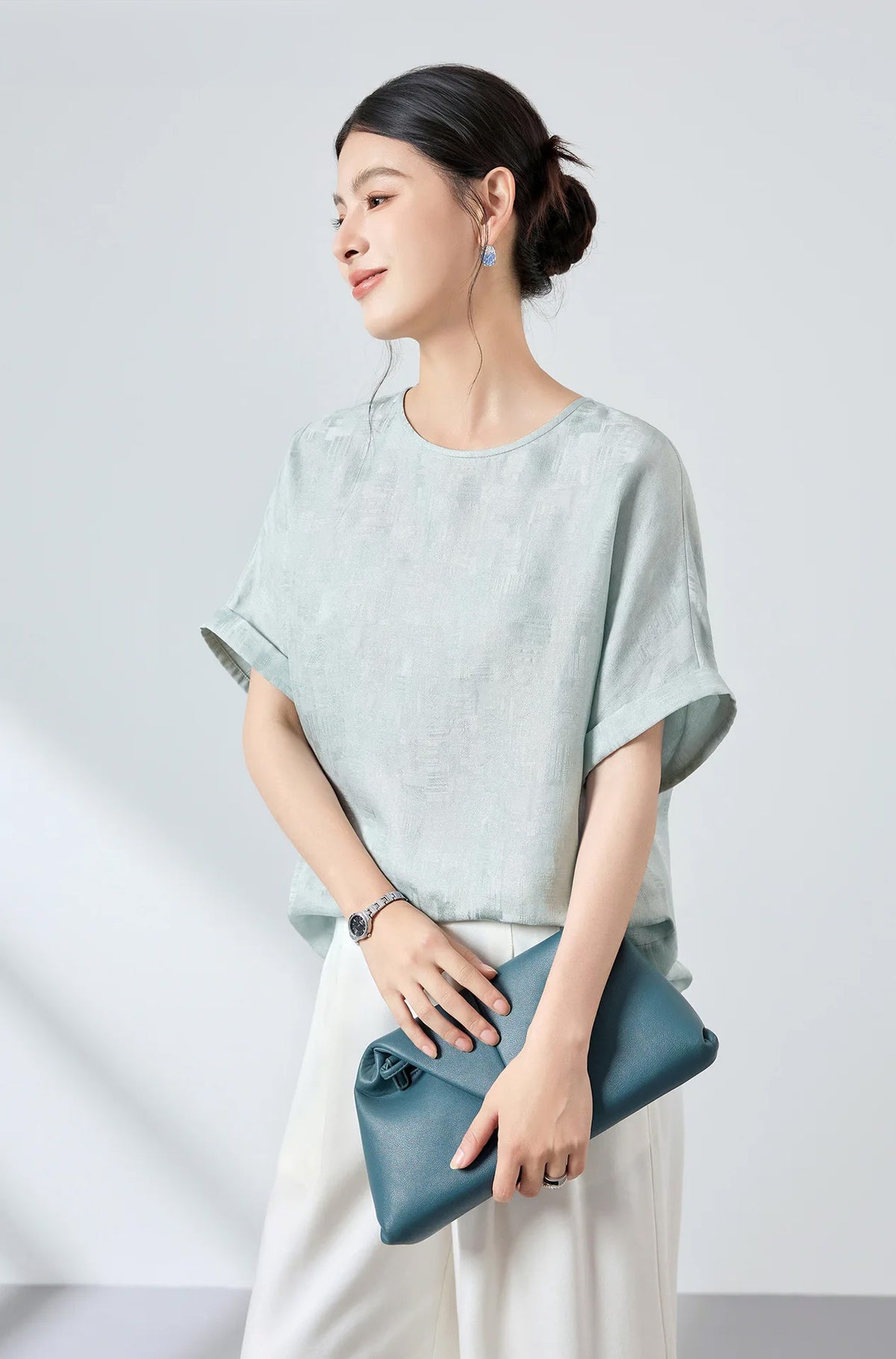 Model wearing a Glacial Spring silk Sangbo jacquard blouse styled with white pants and holding an elegant blue clutch — From Borcelleclothes.