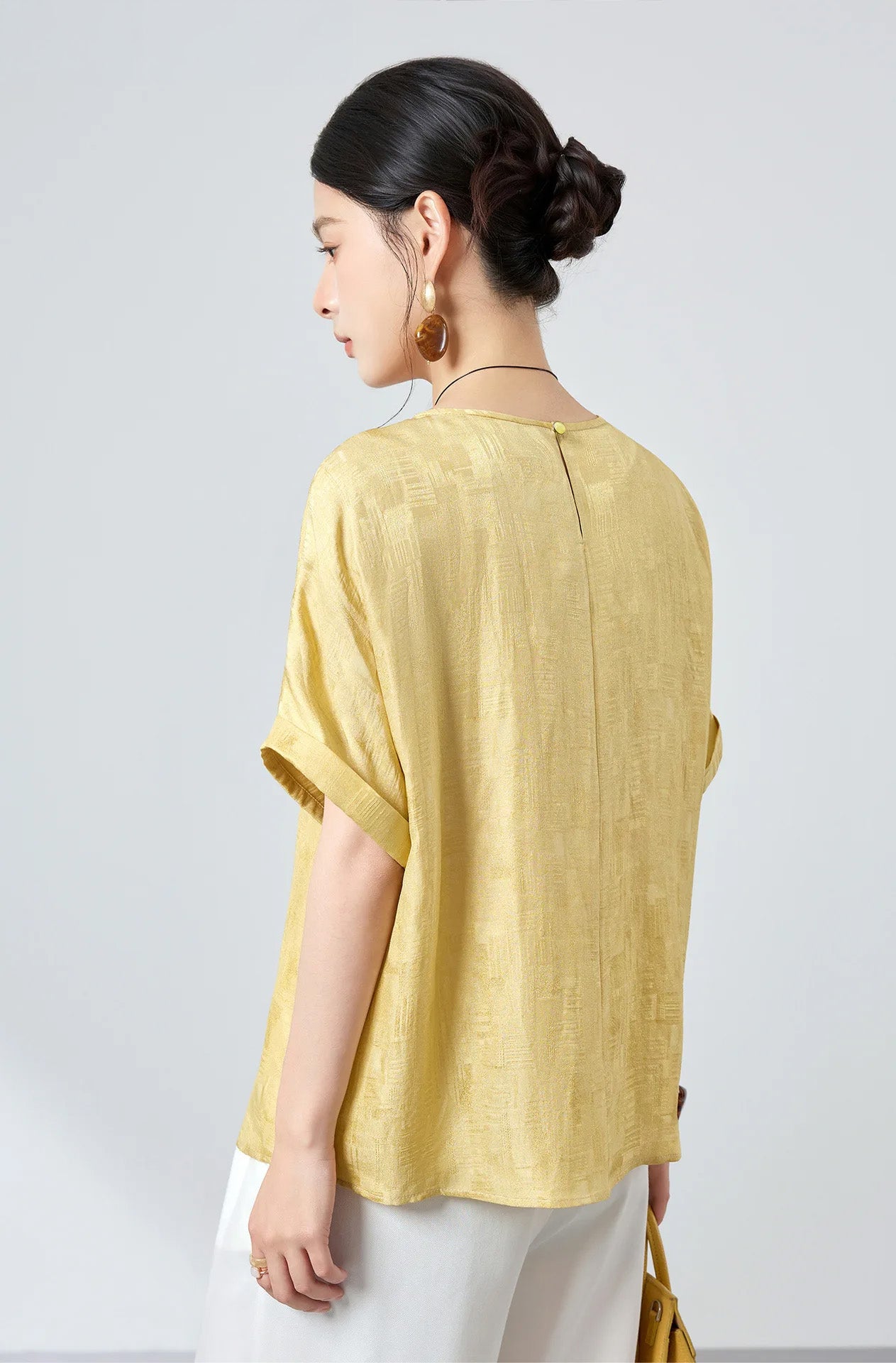 Back view of model wearing a women's Hakea Mulberry silk Sangbo jacquard blouse highlighting its clean shoulder line and fluid drape — From Borcelleclothes.