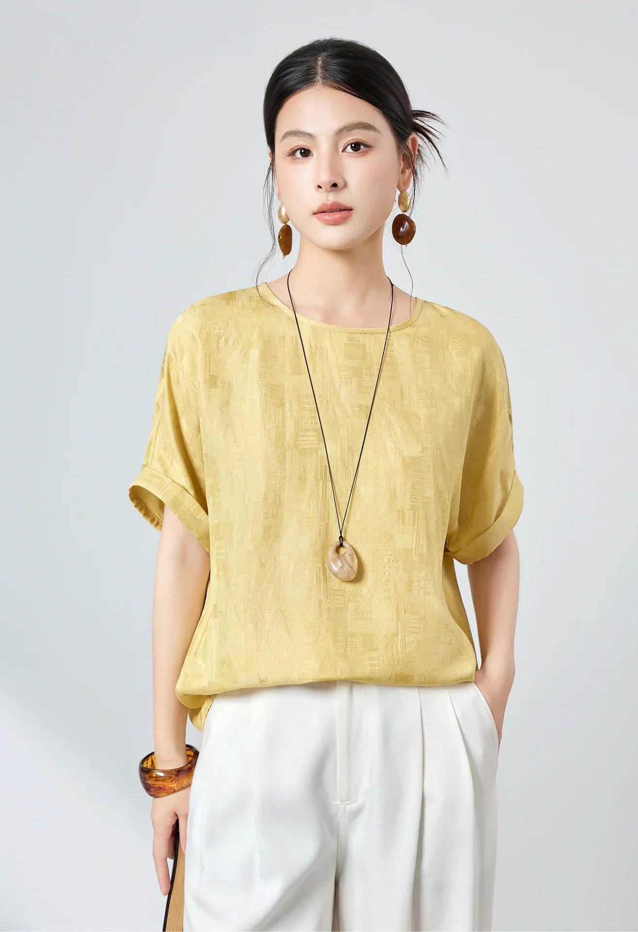 Side view of model wearing a Hakea silk Sangbo blouse paired with white tailored trousers, one hand in pocket — From Borcelleclothes.