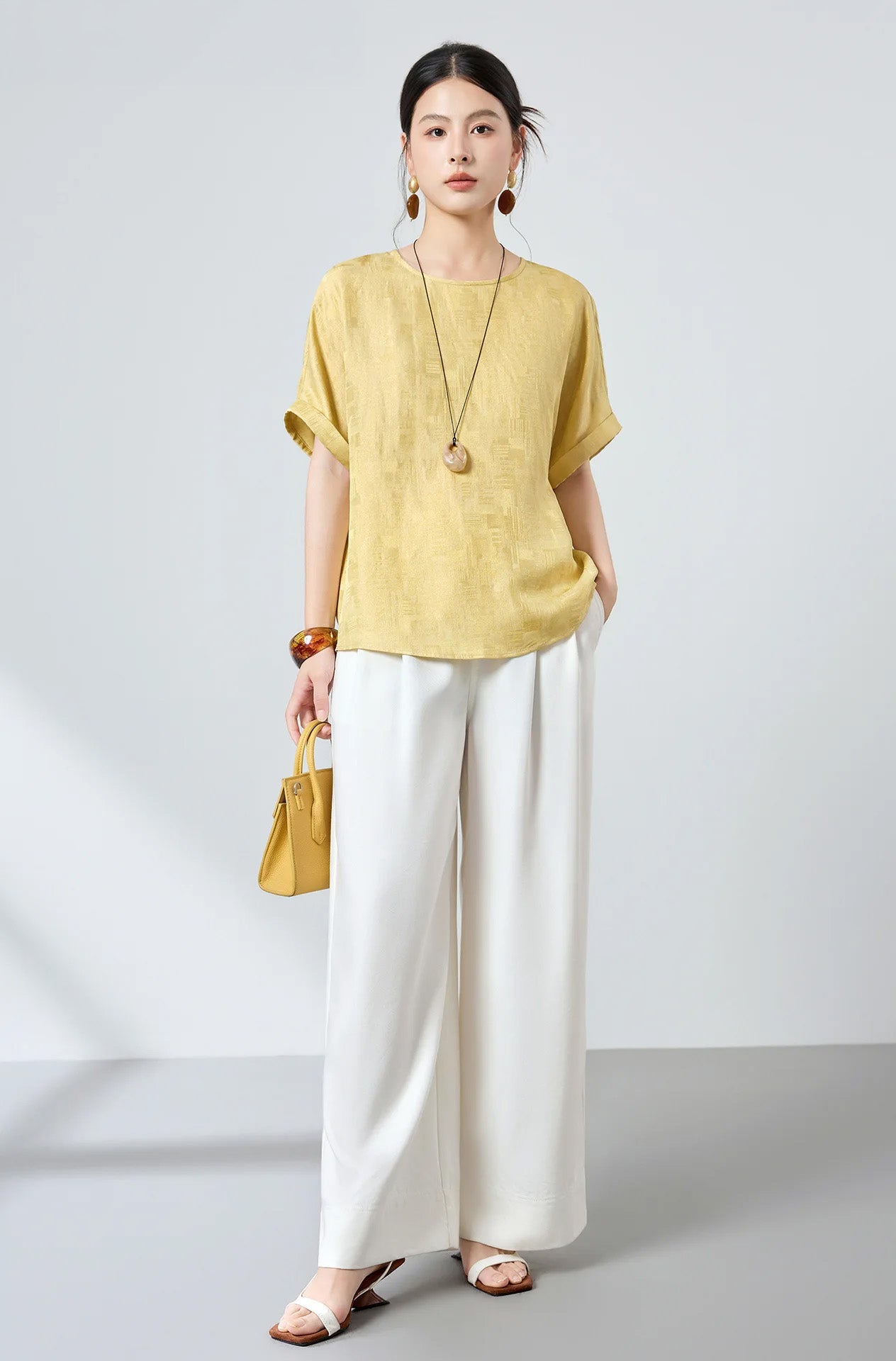Model wearing an elegant Hakea silk Sangbo jacquard blouse styled with  white pants and a yellow handbag — From Borcelleclothes.