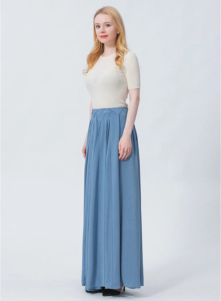 Full-height studio shot of a model turned slightly to the side, showcasing the majestic drape and fluid, aqueous movement of the gathered arched inset panels in premium blue silk. — From Borcelleclothes.