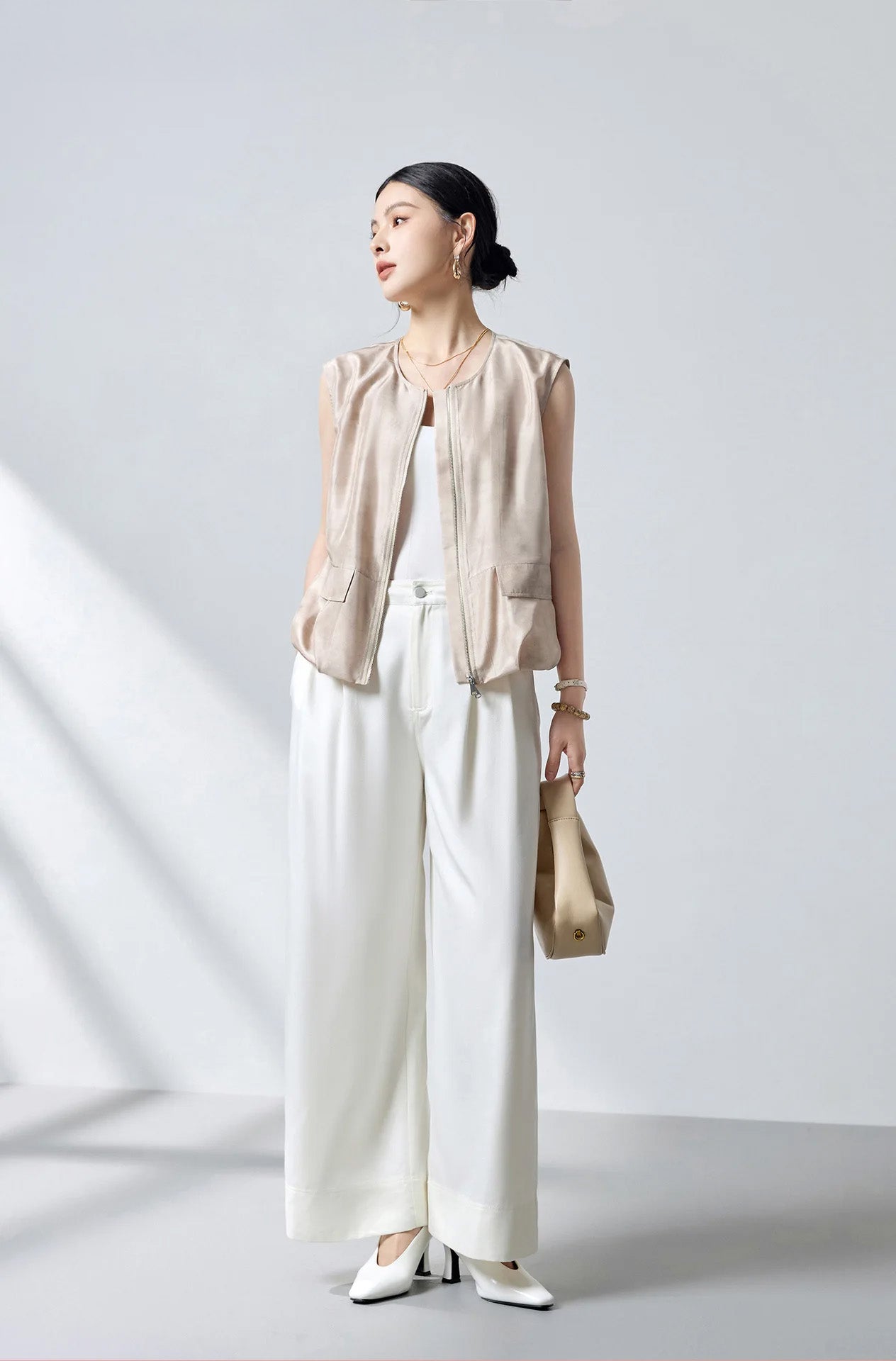 Model styled in white pants holding a handbag wearing the sleeveless Mulberry silk blouson jacket in Whispering Wind — From Borcelleclothes.