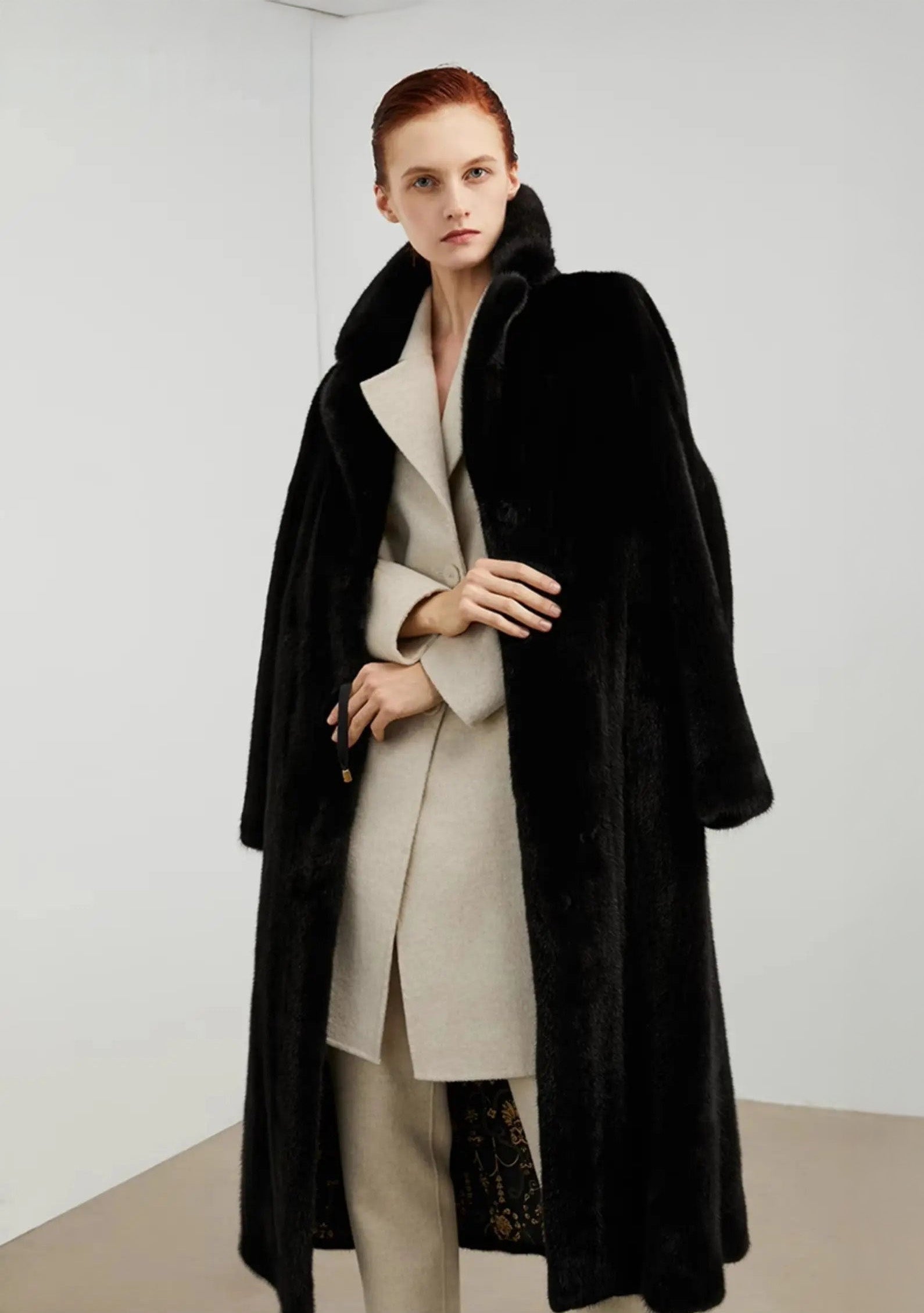 Model wearing an unfastened straight-cut mink coat in rich black, holding the front edges of the garment — From Borcelleclothes.