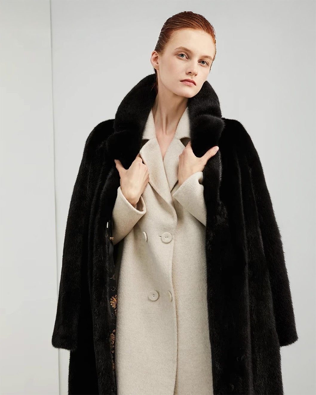 Model wearing a straight mink coat in rich black, unfastened, gently holding the lapels — From Borcelleclothes.