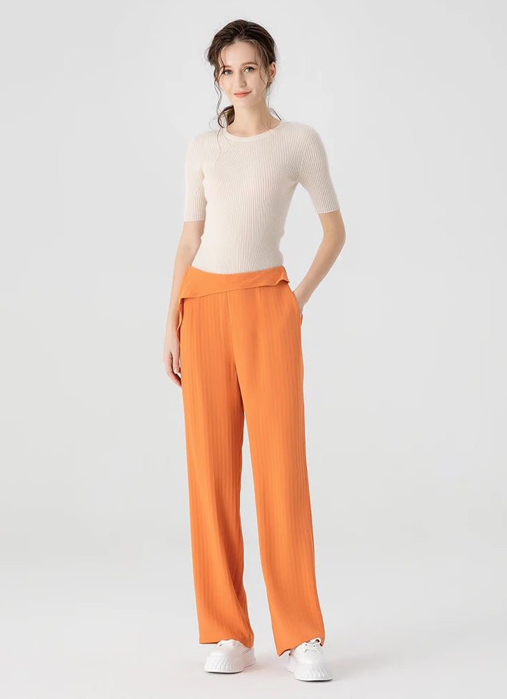 Full-height shot of a woman in orange silk jacquard tapered trousers with a hand in the side pocket, showcasing the fluid silhouette — From Borcelleclothes.