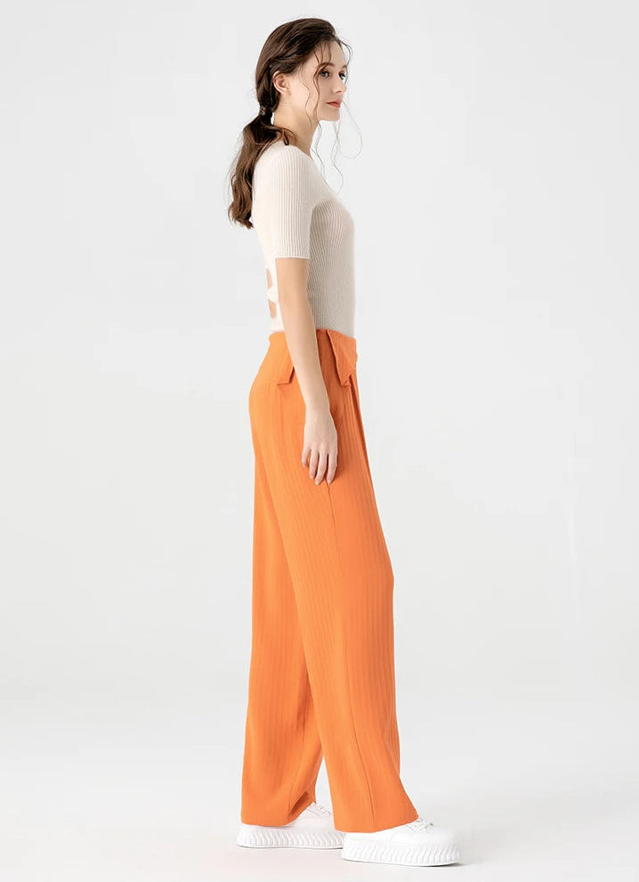 Full-height left side profile of a woman in high-density Mulberry silk tapered trousers in vibrant gradient orange — From Borcelleclothes.