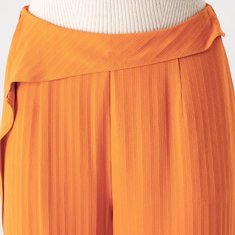Close-up front view of the upper waist section on orange silk trousers, featuring an asymmetrical overlay sculpted with a single fixed pleat — From Borcelleclothes.