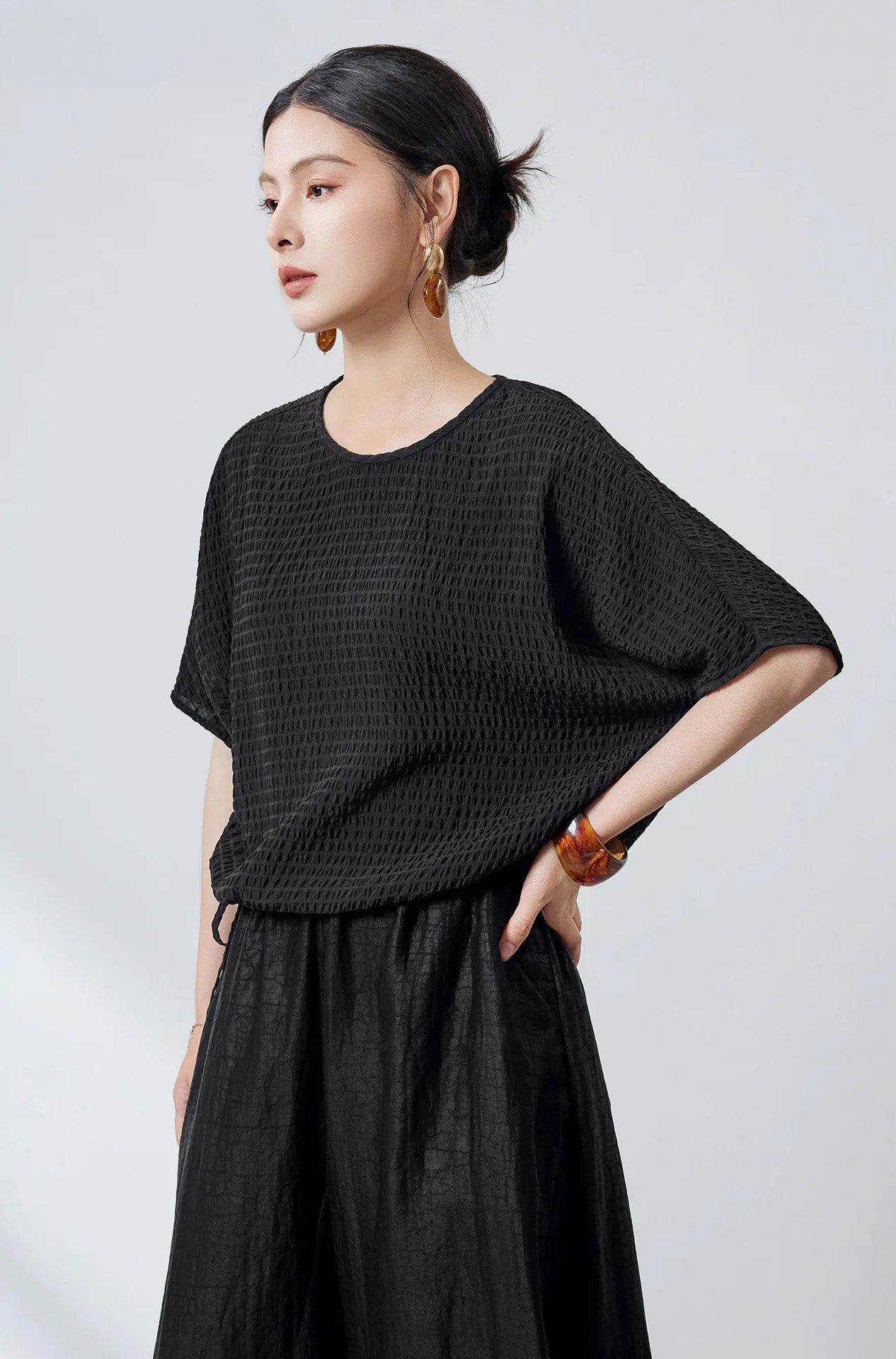 A woman posing with one hand on her hip wearing a black textured silk blouse — From Borcelleclothes.