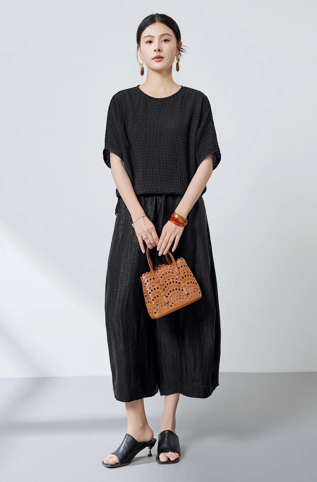 A woman holding a handbag with both hands while wearing a loose-fit black Mulberry silk blouse — From Borcelleclothes.
