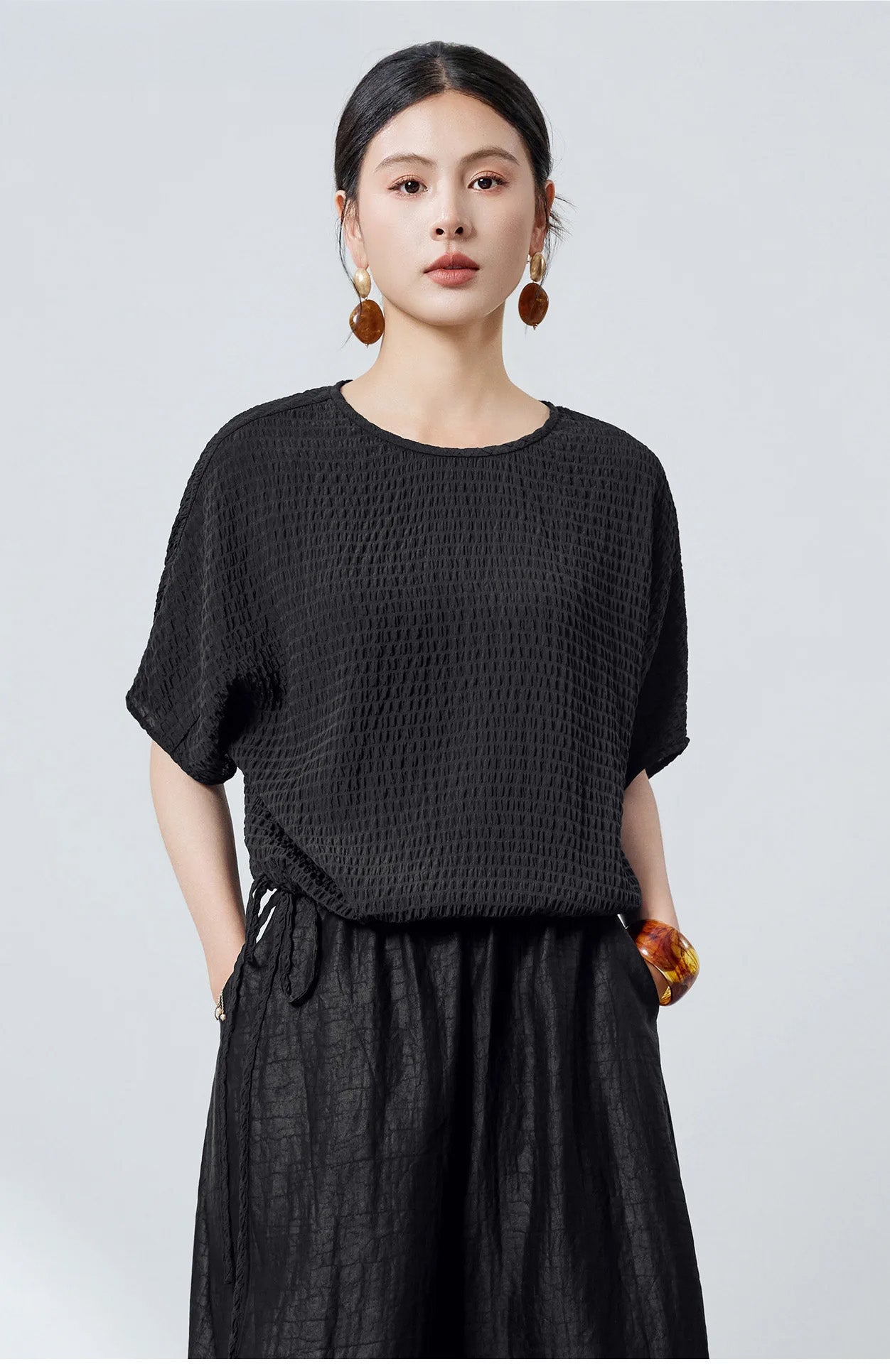 A woman standing in a black textured Mulberry silk blouse with her hands in her pants pockets — From Borcelleclothes.