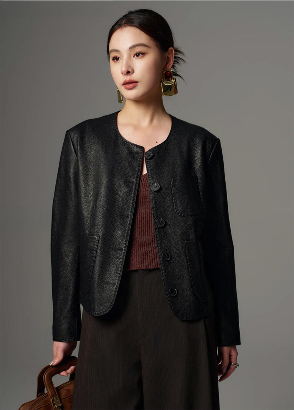 Model holding a handbag while wearing the cropped pebble goatskin jacket in Calculated Tension — From Borcelleclothes.