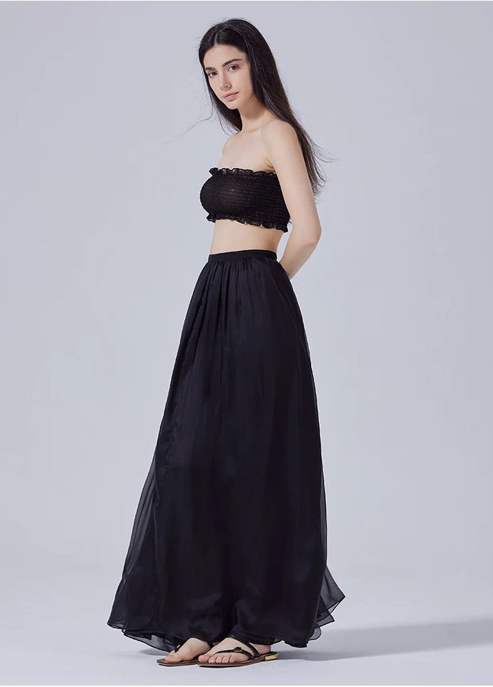 Model turned slightly to the side with arms behind back, showing pleated silk chiffon skirt silhouette — From Borcelleclothes.