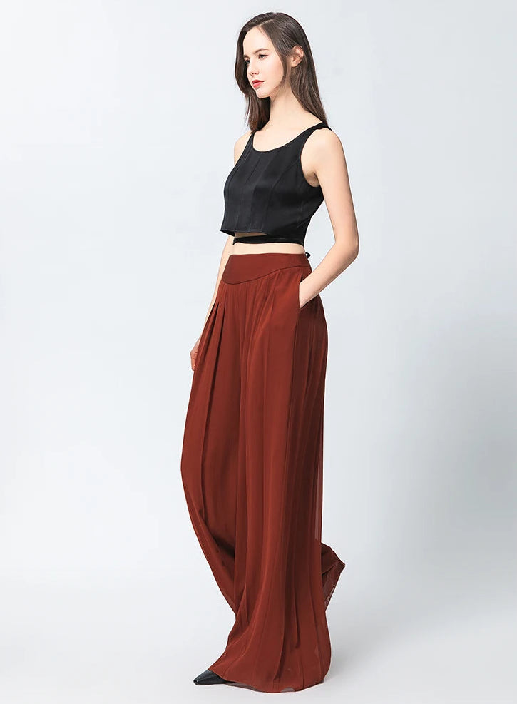 Side view of two-layer pleated Mulberry silk georgette trousers in Contradictory Terracotta with model's hand in pocket — From Borcelleclothes.