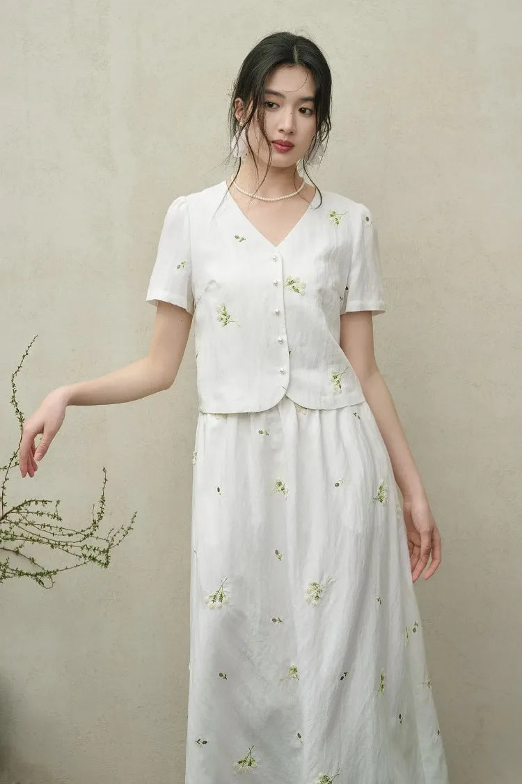 A woman in the Utsugi Blossom viscose set, Bride’s Silence white, looking thoughtfully to the side with a gently bent arm, showcasing the elegant flow of the fabric — From Borcelleclothes.