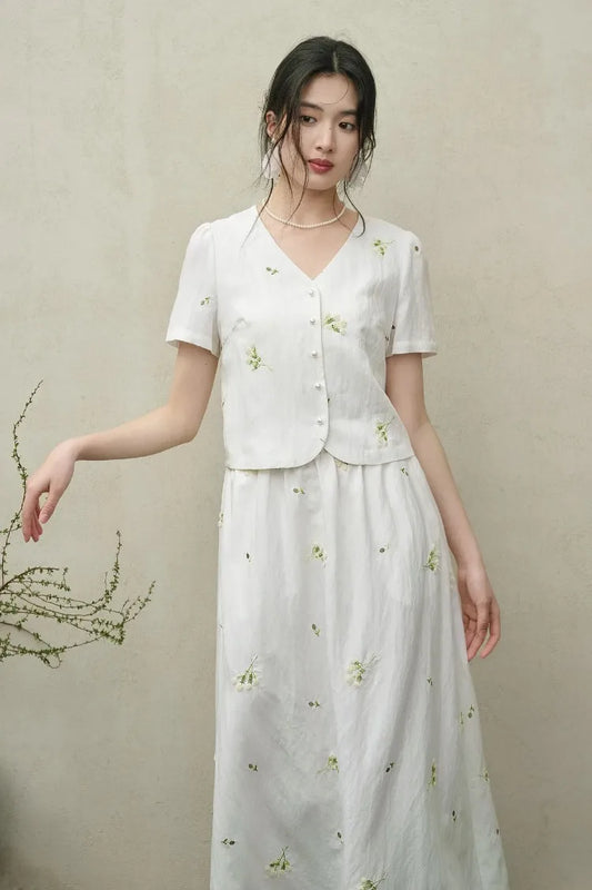 A woman in the Utsugi Blossom viscose set, Bride’s Silence white, looking thoughtfully to the side with a gently bent arm, showcasing the elegant flow of the fabric — From Borcelleclothes.