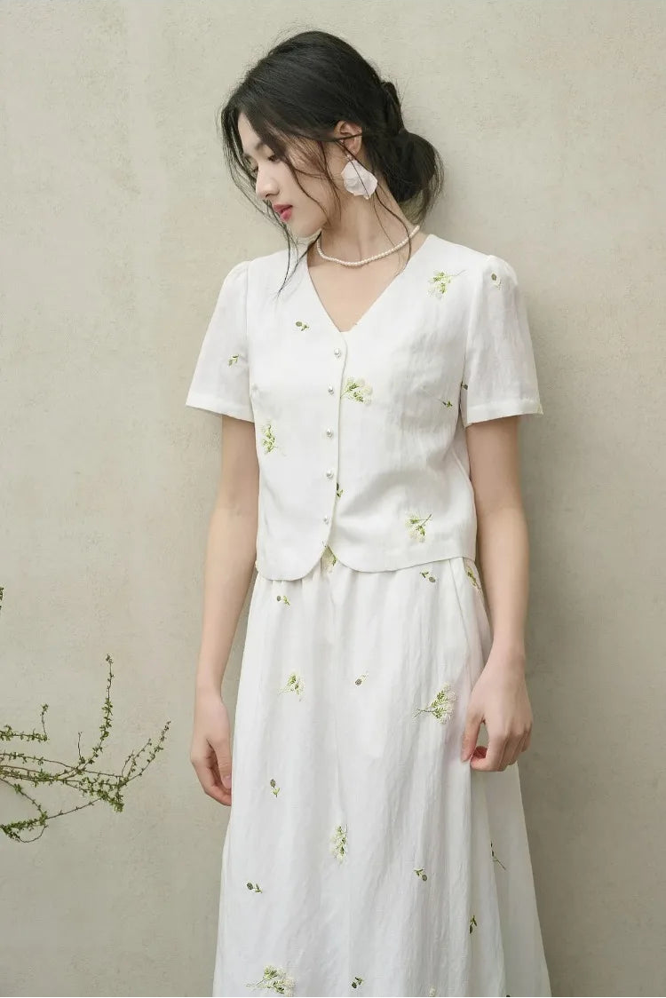 A serene moment of a woman in the Utsugi Blossom set looking down, highlighting the soft V-neckline and the delicate Bride’s Silence white palette — From Borcelleclothes.