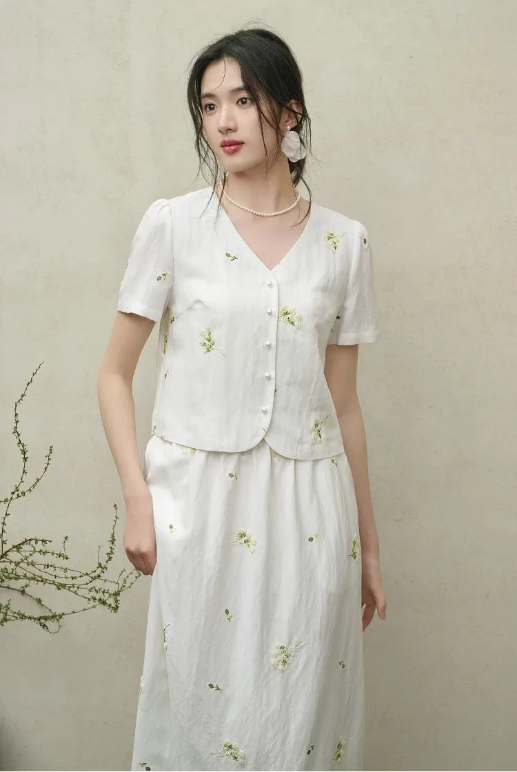 A woman gently touching the hem of her Utsugi Blossom skirt while looking away, emphasizing the tactile nature of the Bride’s Silence white fabric — From Borcelleclothes.