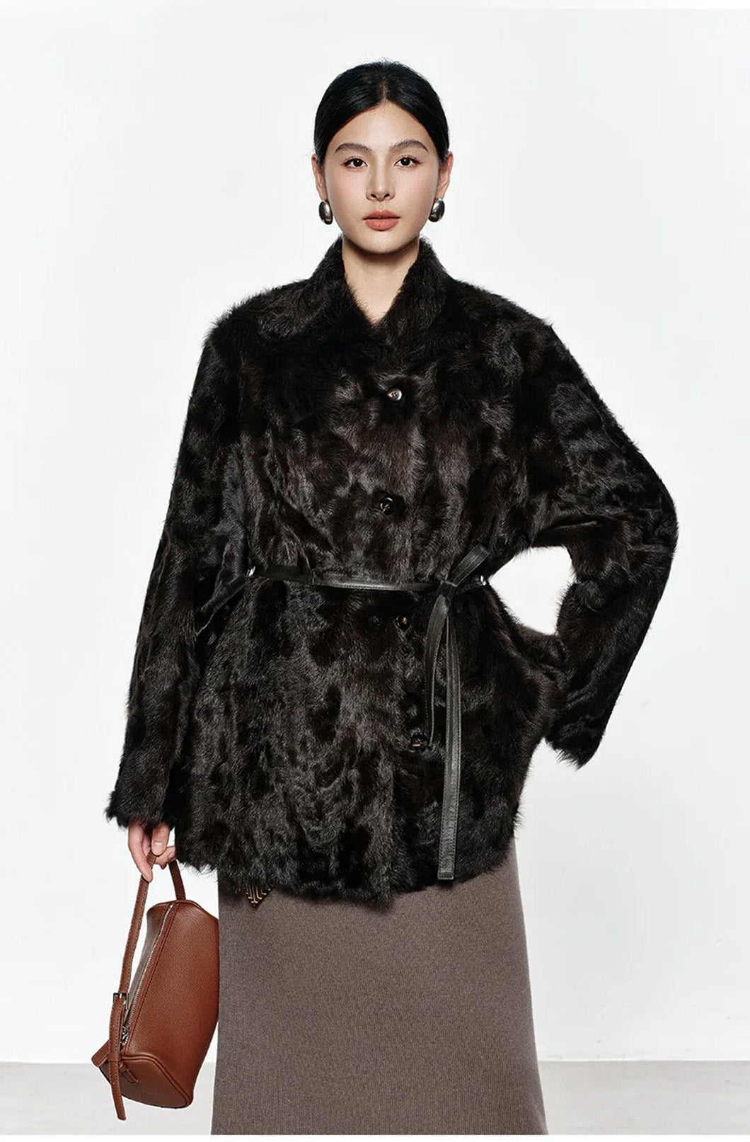 Model lifting the hem of the Henna Glow shearling coat while holding a bag in hand — From Borcelleclothes.