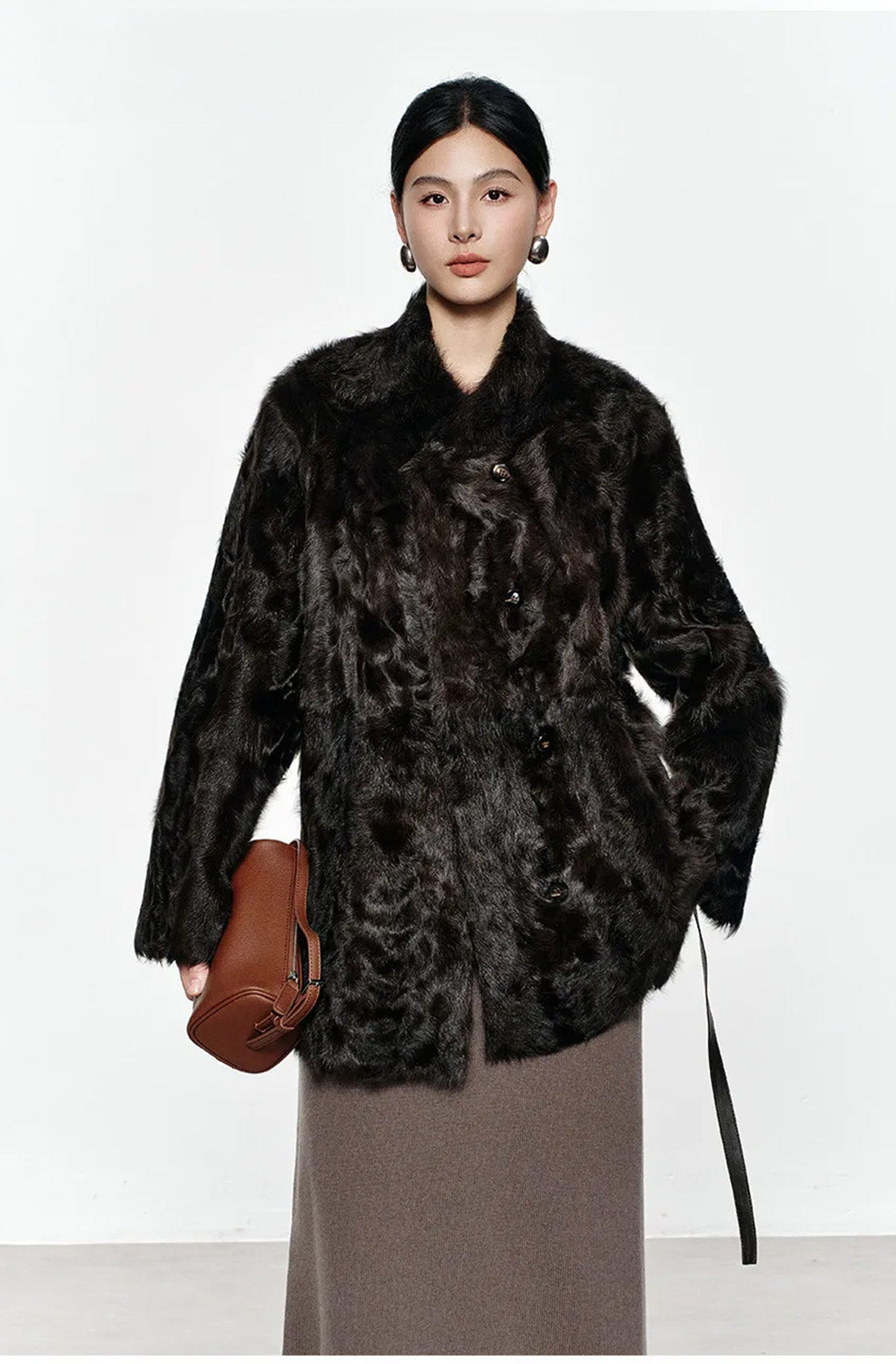Model gently lifting the hem of the Henna Glow shearling coat, revealing the soft double-faced structure — From Borcelleclothes.