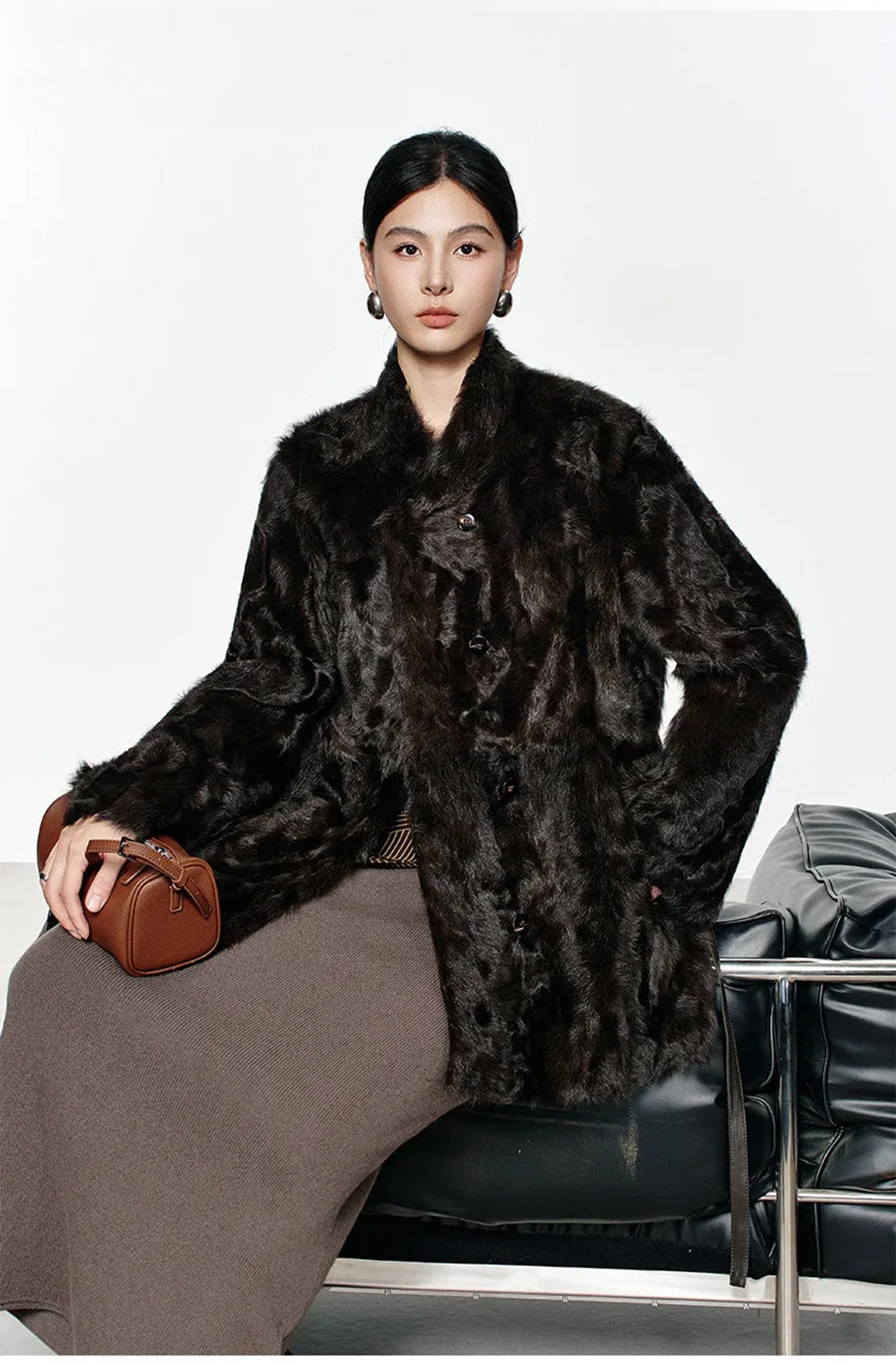 Model seated on a couch wearing the Henna Glow shearling coat, highlighting the natural drape and warm tone — From Borcelleclothes.