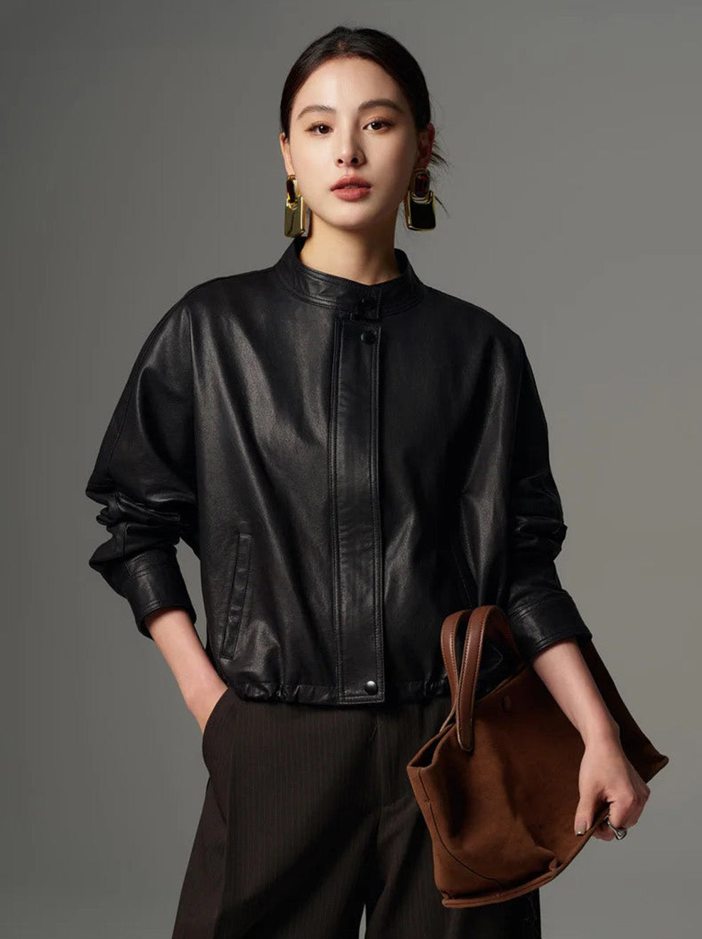 Model styling the Ti Guardo Adesso black leather jacket while holding a slouchy brown suede bag — From Borcelleclothes.