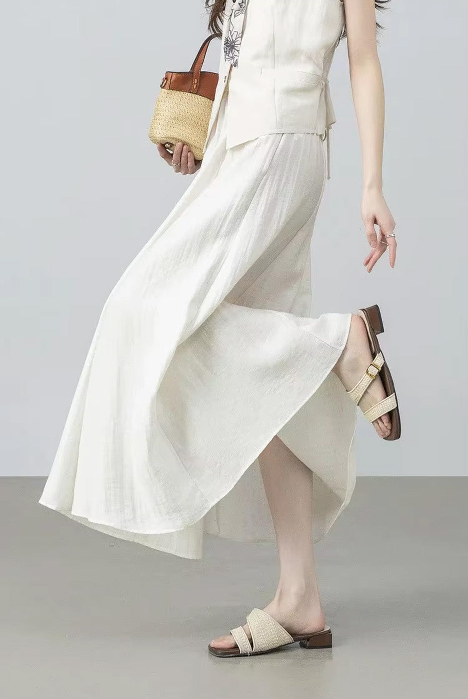 Full-length shot of a model bending down to adjust her sandal, styled with the flowing gathered midi skirt in Azir Fog — From Borcelleclothes.
