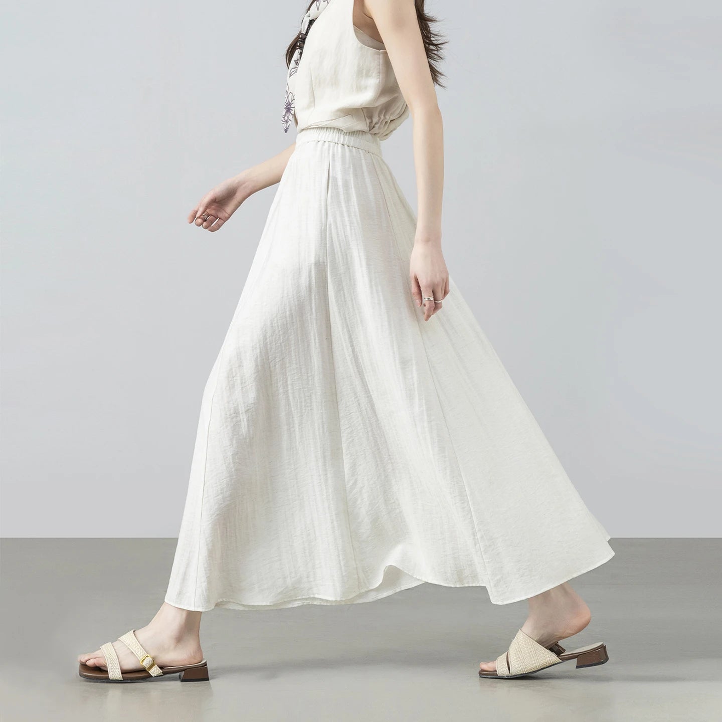Side view of a model walking in the fluid, flared viscose blend gathered midi skirt in Azir Fog — From Borcelleclothes.