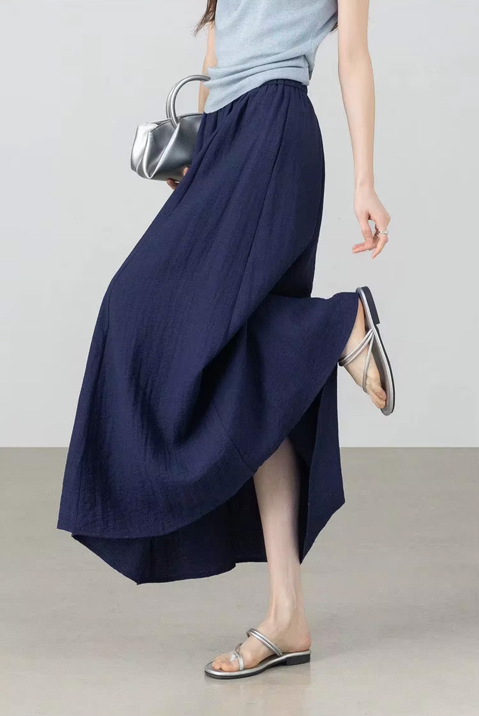 Model reaching down toward her sandals, wearing the relaxed-fit crinkled texture midi skirt in Shurima Oasis — From Borcelleclothes.