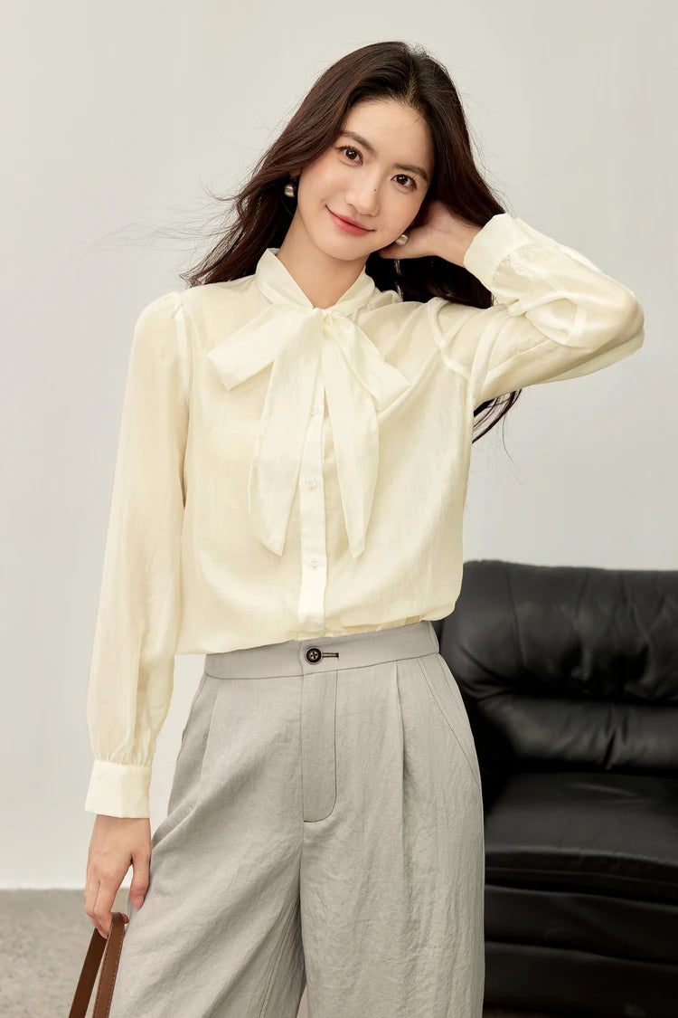 A woman in a semi-sheer elderflower blouse adjusting her loose hair, capturing a moment of spring freshness — From Borcelleclothes.