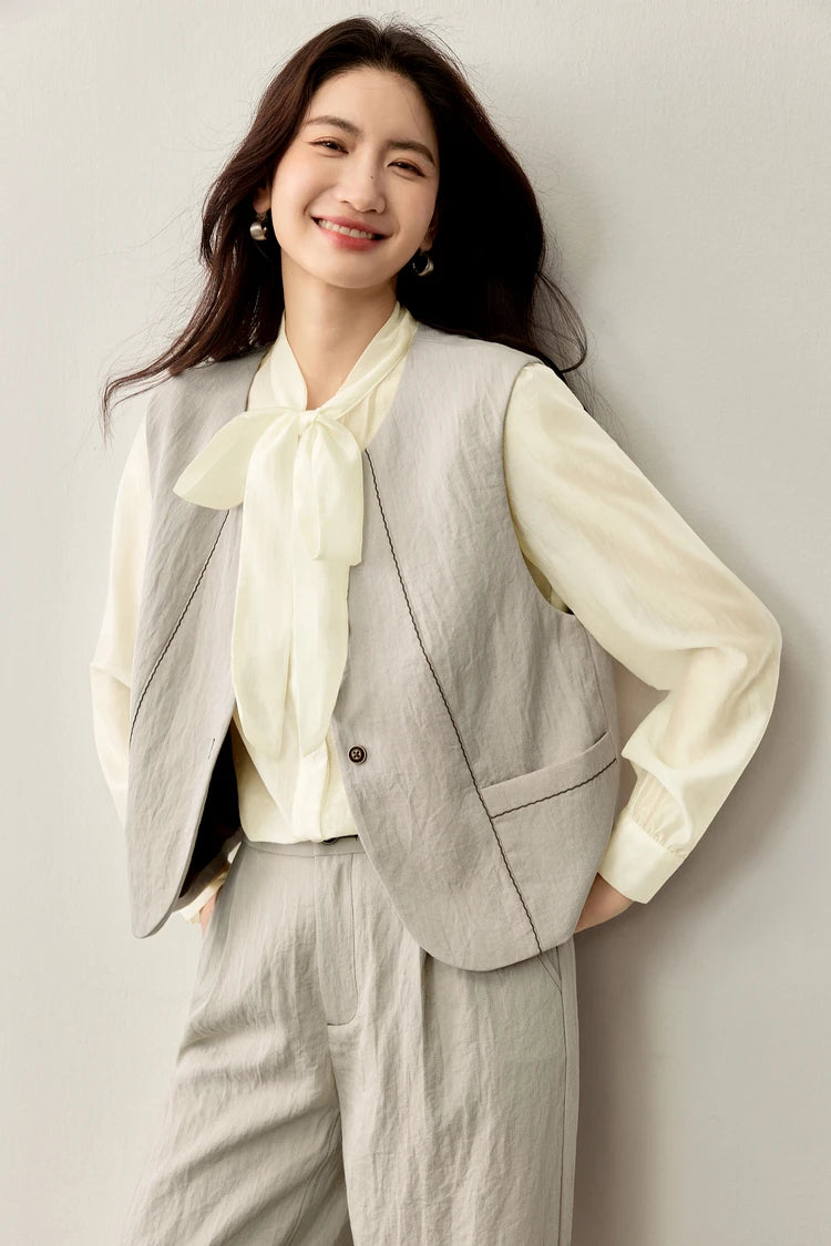 Close-up of a woman in an unbuttoned truffle vest, revealing the delicate textures of the elderflower blouse — From Borcelleclothes.