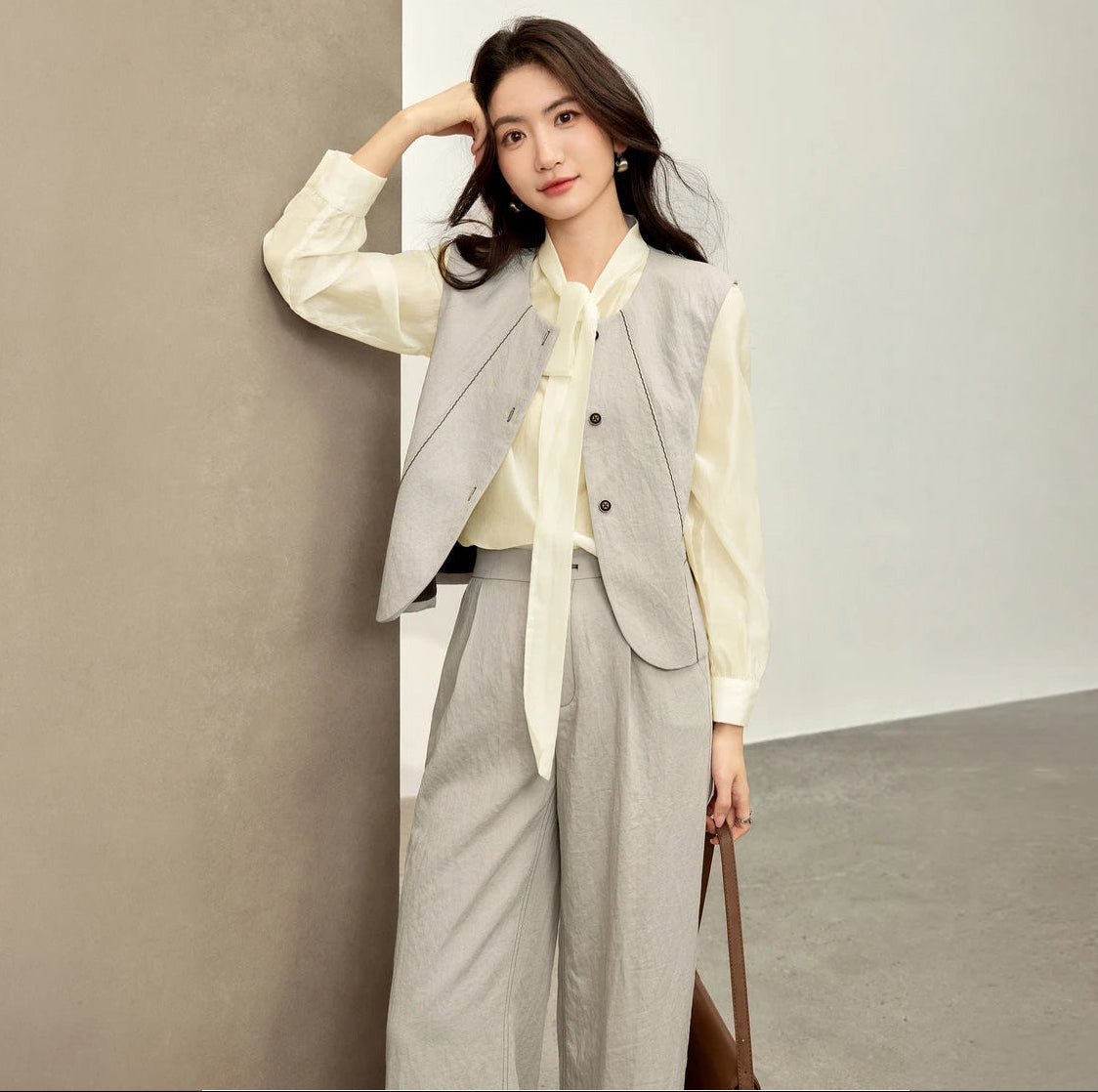 Women's three-piece suit made of textured chocolate truffle viscose, featuring a deep round neckline vest with wave-stitch embroidery, straight-leg pleated trousers, and a lightweight semi-sheer blouse in elderflower shade with a transformable bow-tie collar. — From Borcelleclothes.