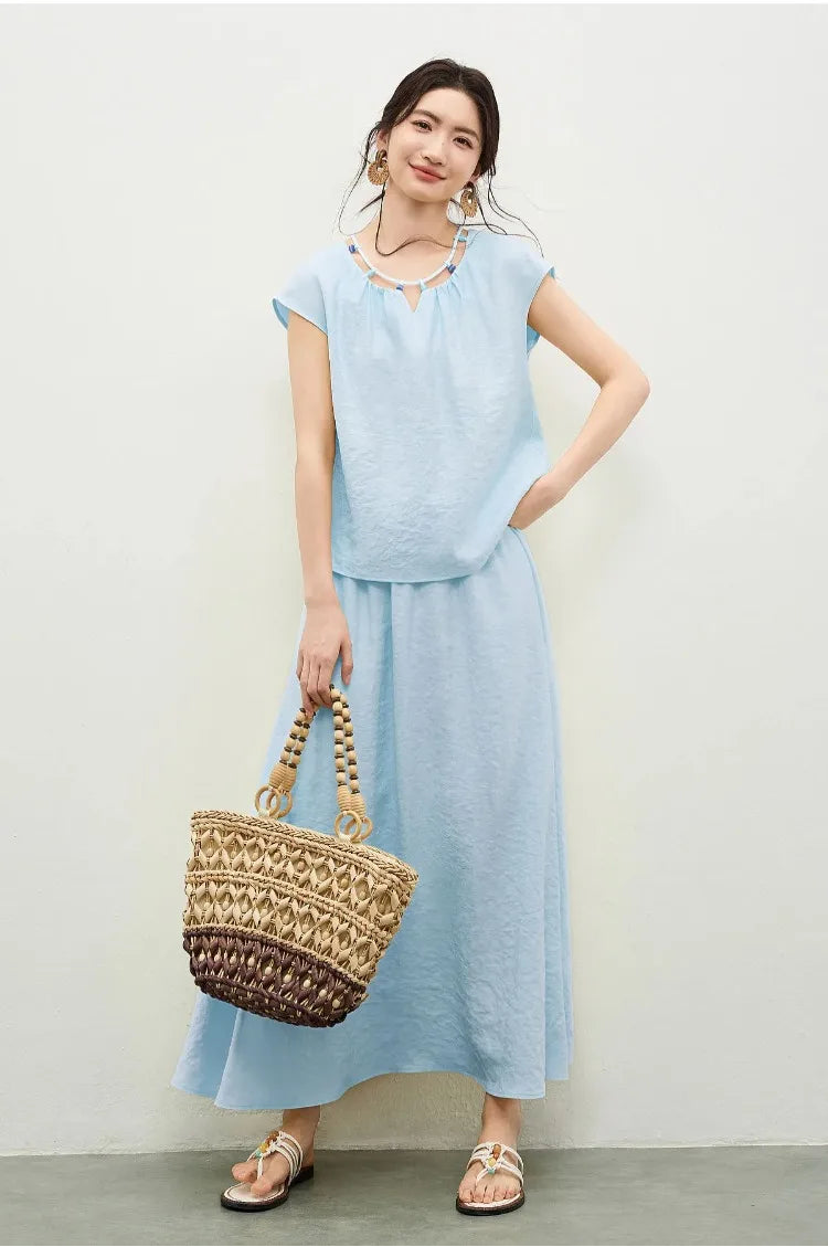 A woman in a sky blue viscose set holding a woven bag, showcasing a relaxed yet sophisticated summer look — From Borcelleclothes.