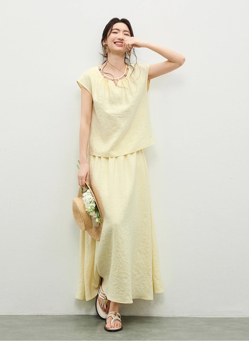 A woman in the yellow viscose set with a gentle smile, touching her lips, framed by the creative beaded necklace detail — From Borcelleclothes.