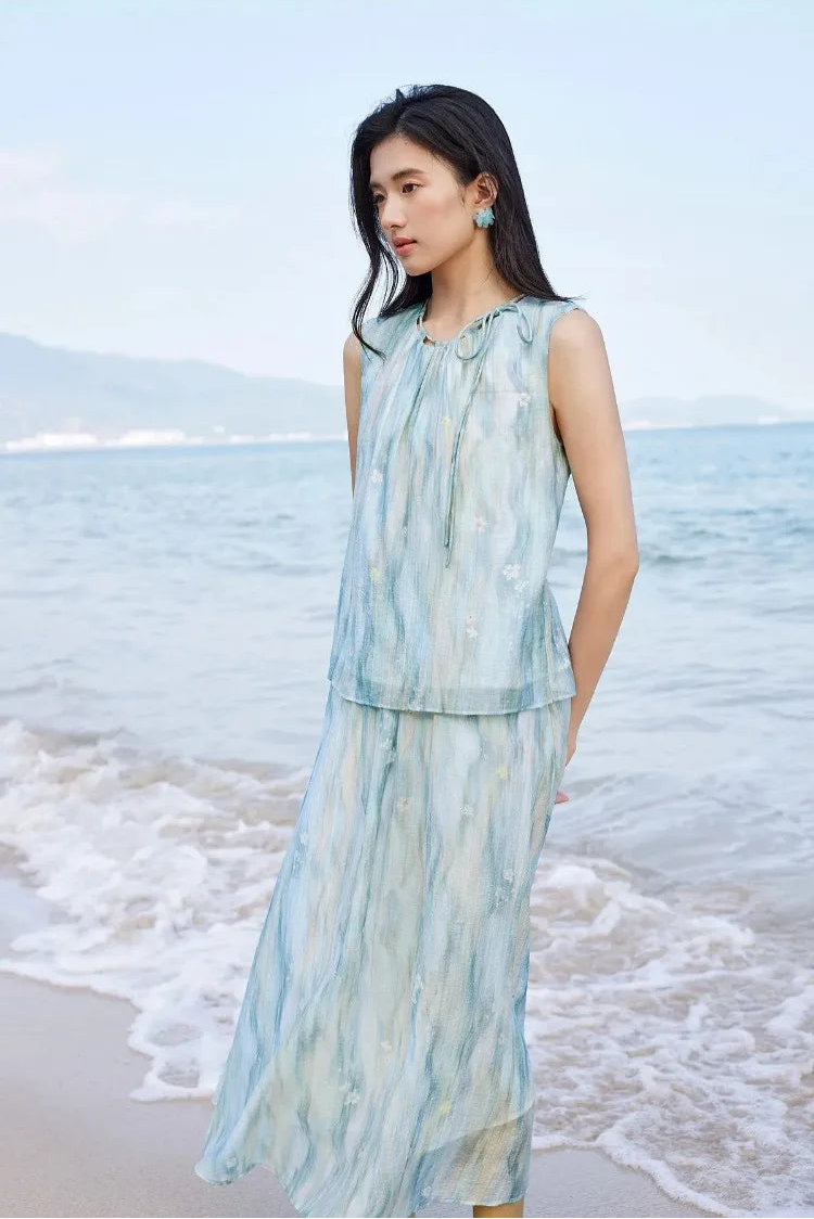 Serene woman posing by the sea in a sleeveless watercolor top and flared skirt — From Borcelleclothes.