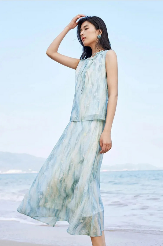 Elegant woman in a watercolor lyocell set gently touching her hair against the sea breeze — From Borcelleclothes.