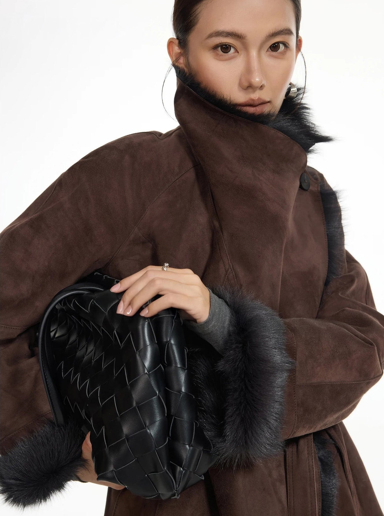 Model holding a bag with both hands, wearing the wide-lapel double-faced goatskin coat in Raw Umber — From Borcelleclothes.