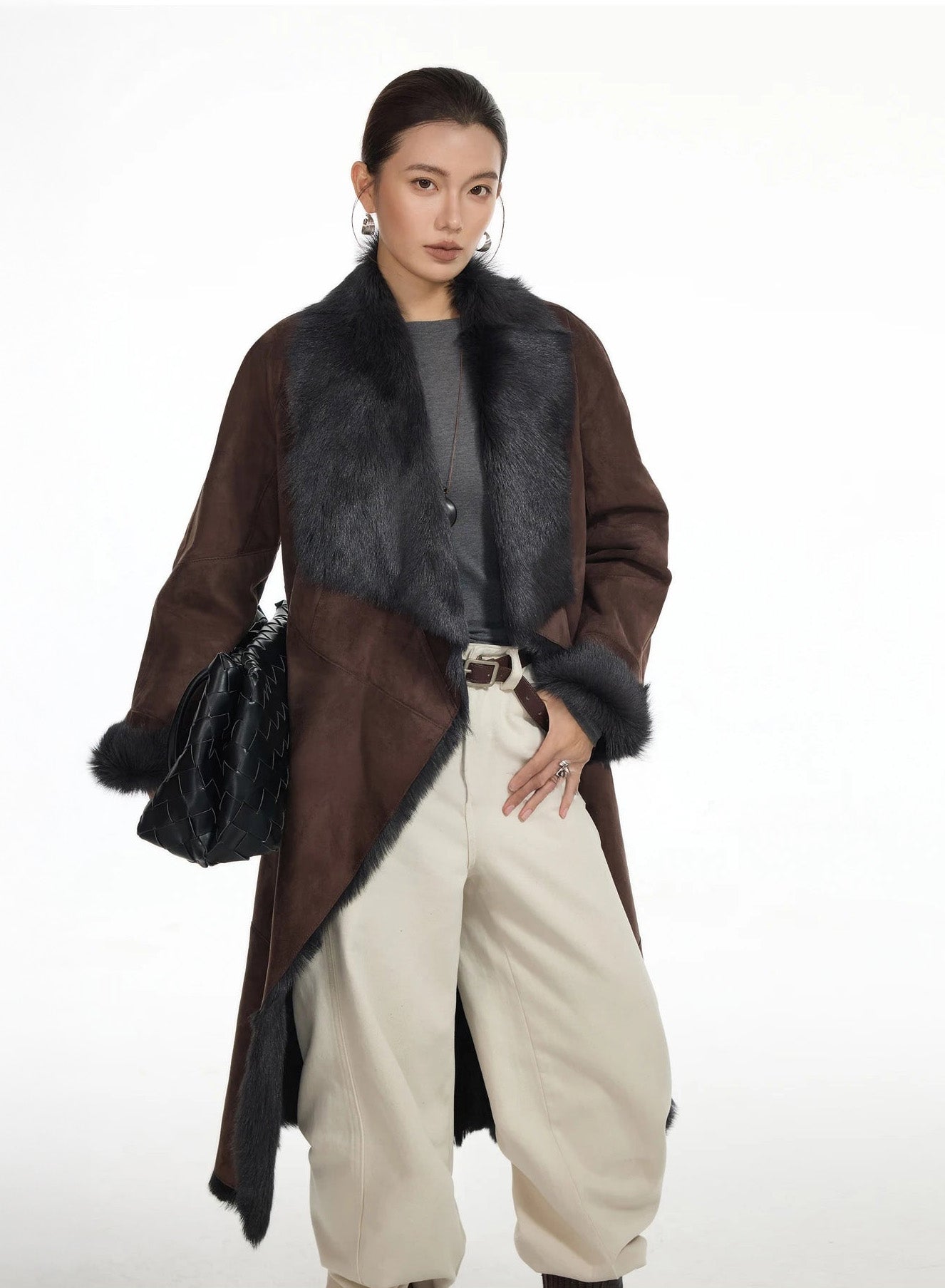 Model holding a bag on hip while wearing the wide-lapel Raw Umber goatskin coat — From Borcelleclothes.