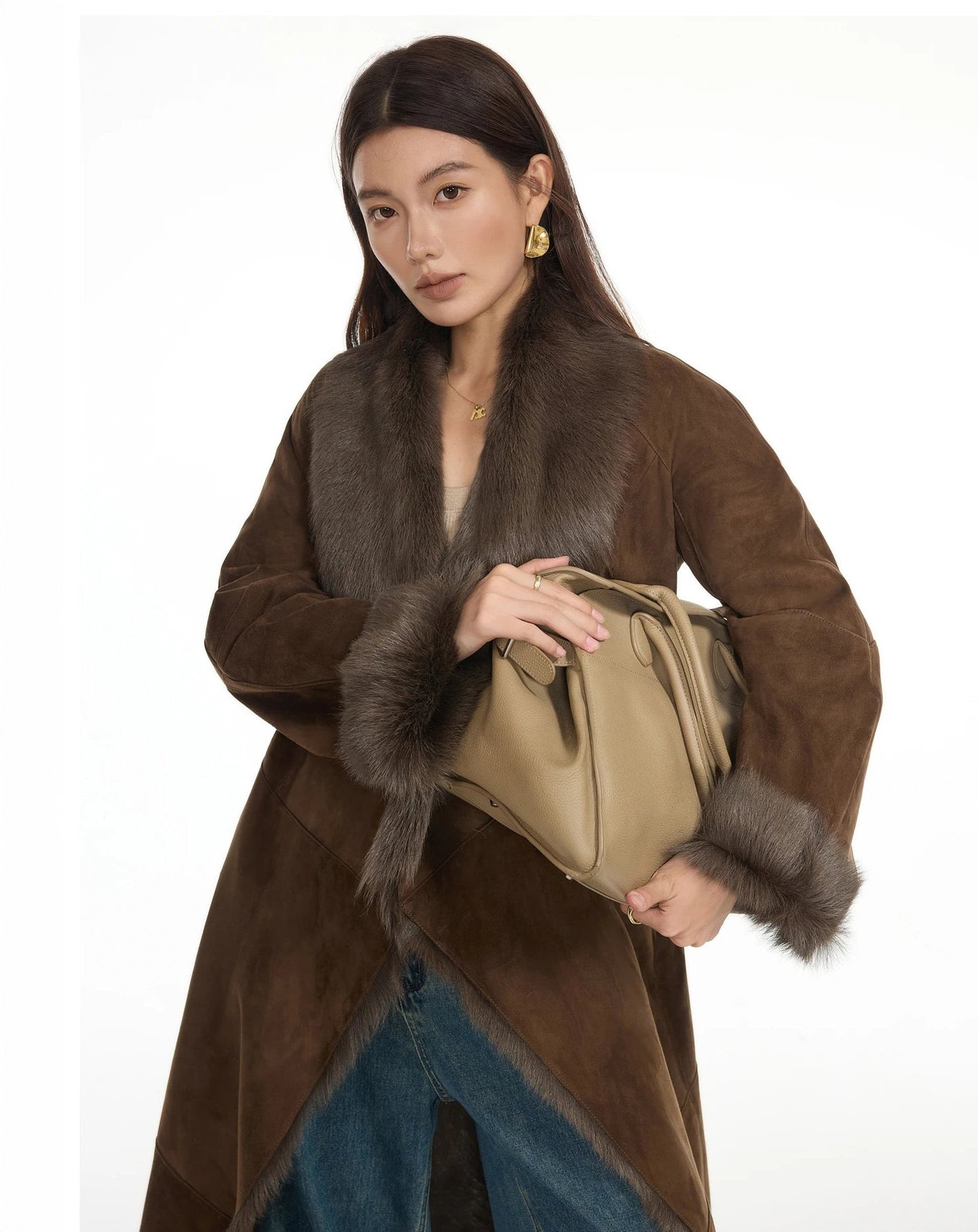 Model holding a structured bag with both hands, wearing the Woodsy Brown wide-lapel goatskin coat — From Borcelleclothes.