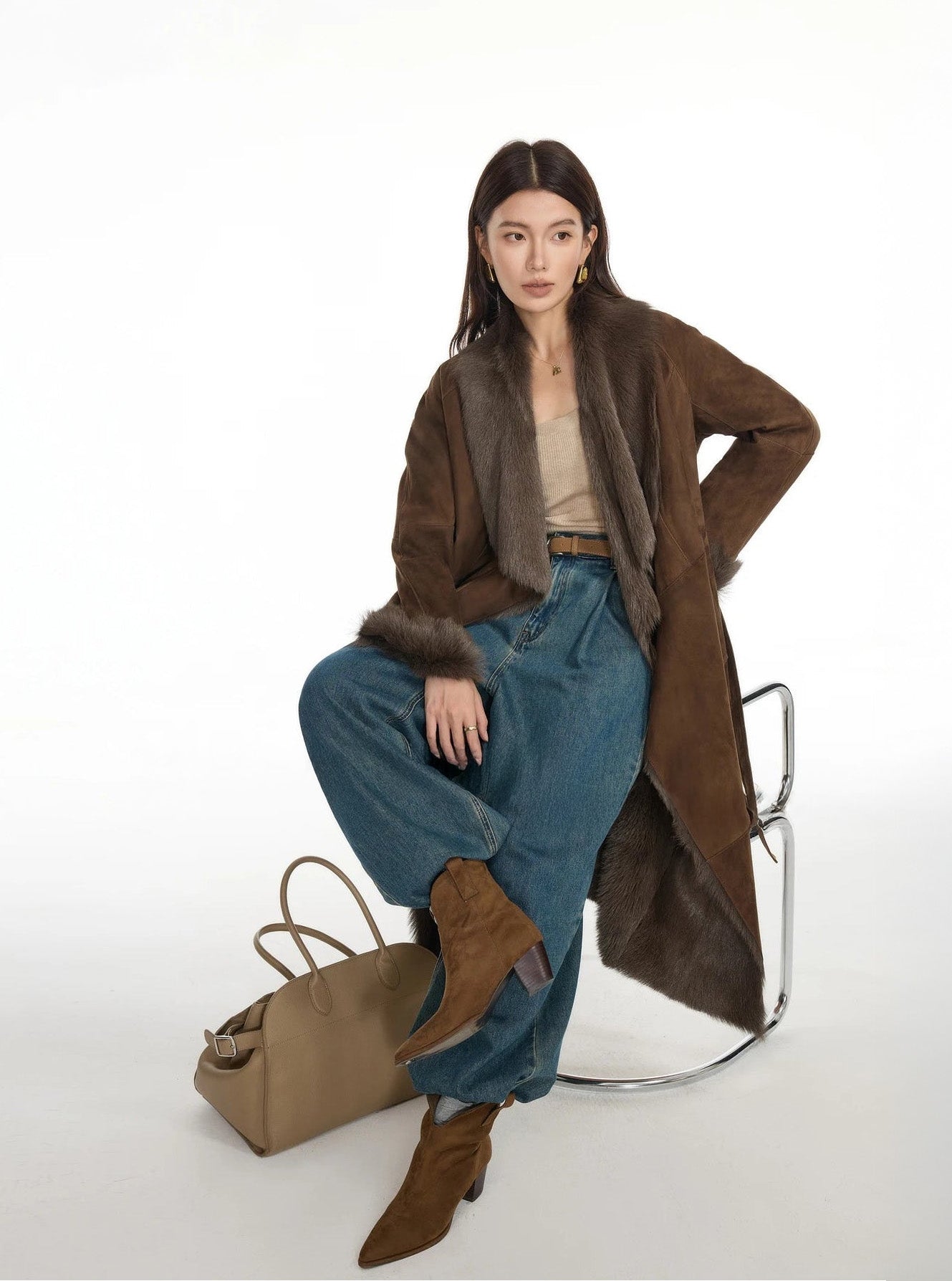Model seated on a chair in a wide-lapel double-faced goatskin coat, styled in Woodsy Brown — From Borcelleclothes.